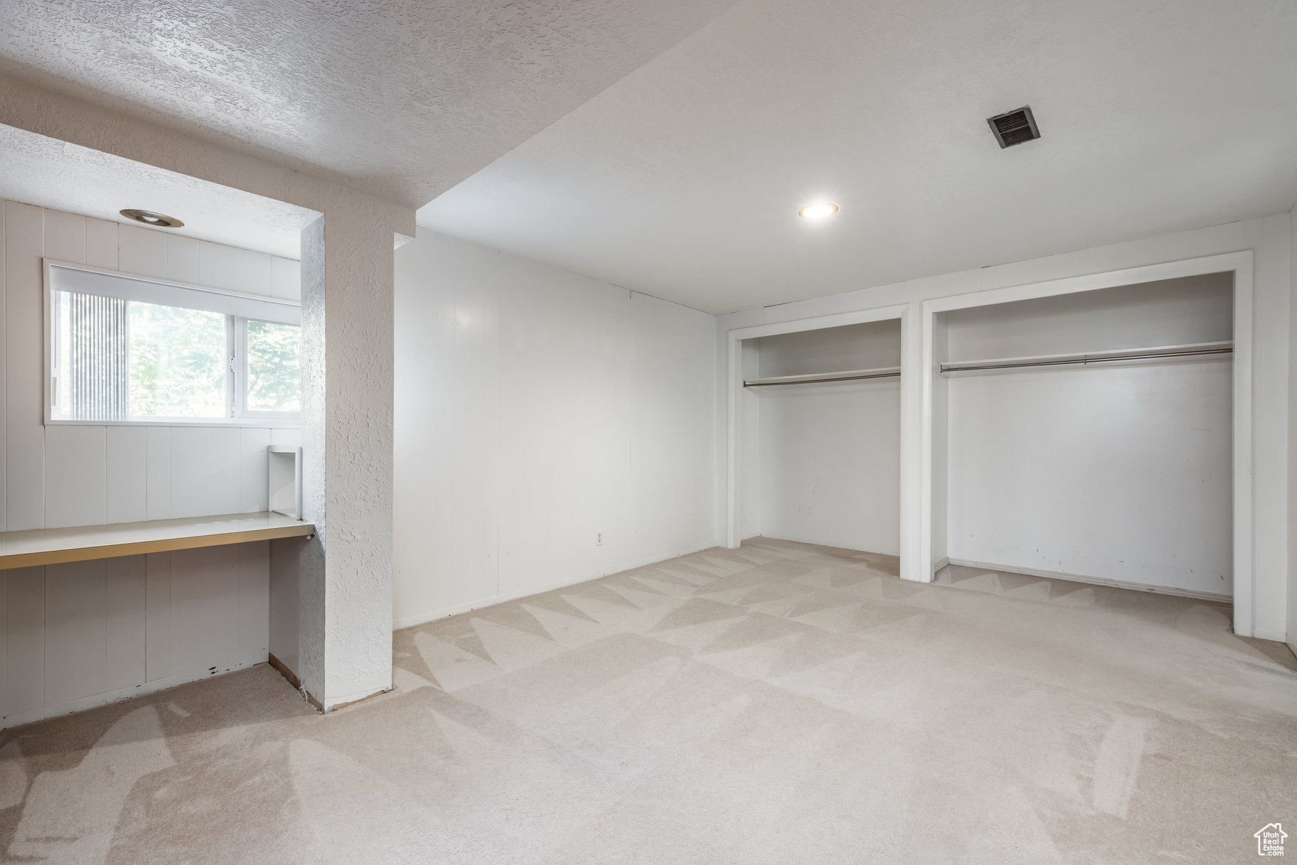 Unfurnished bedroom featuring light colored carpet, built in desk, a textured ceiling, and multiple closets