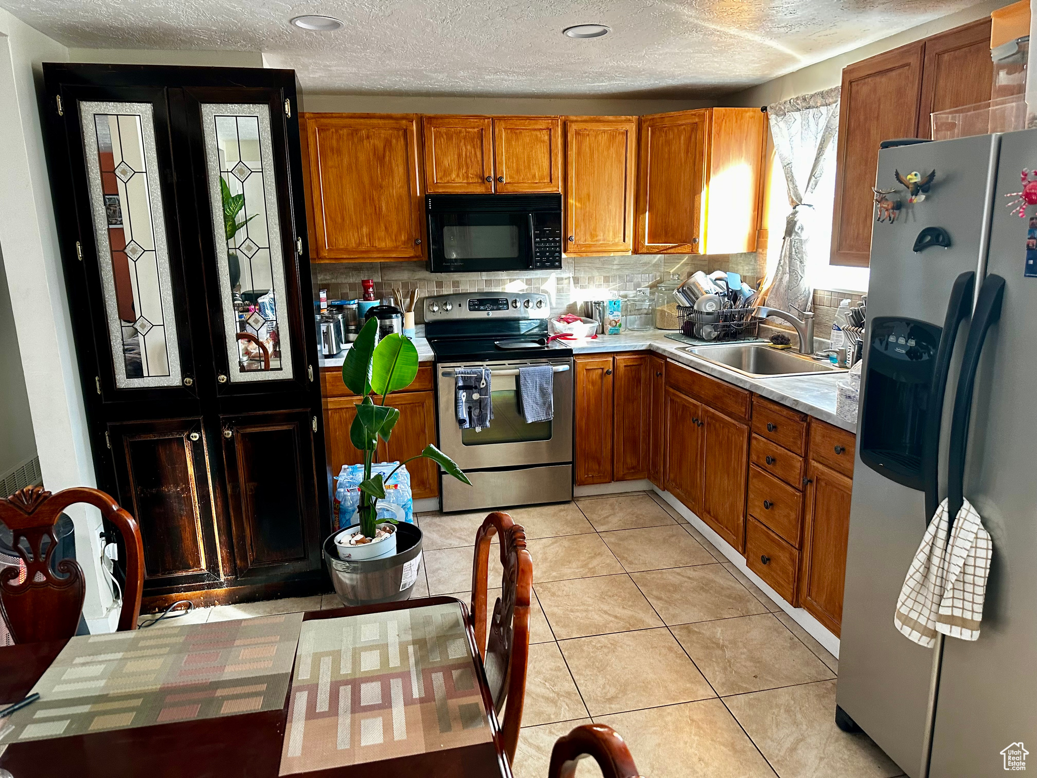 Kitchen featuring appliances with stainless steel finishes, tasteful backsplash, a textured ceiling, sink, and light tile patterned floors