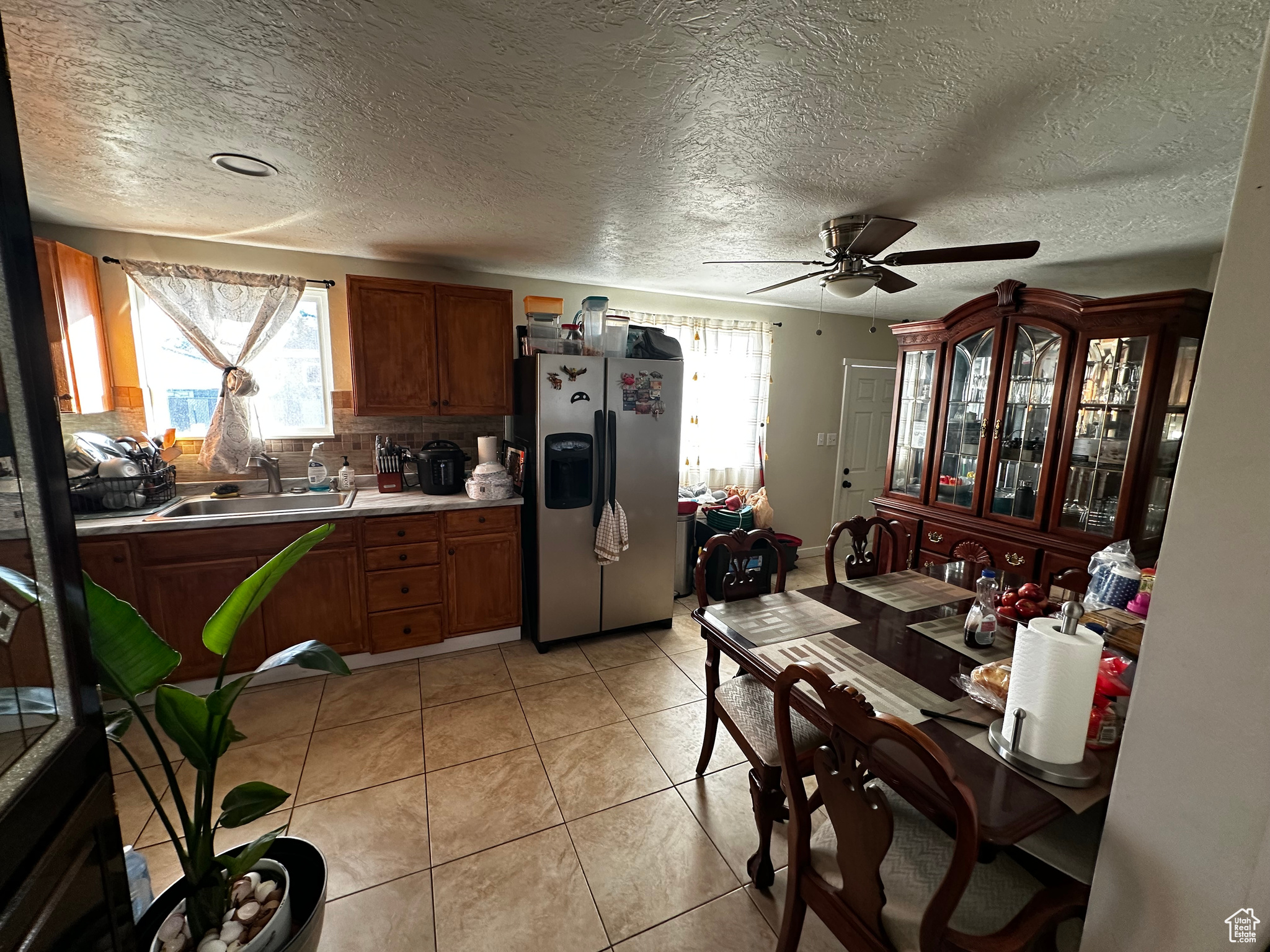 Kitchen with sink, ceiling fan, light tile patterned floors, tasteful backsplash, and stainless steel fridge with ice dispenser