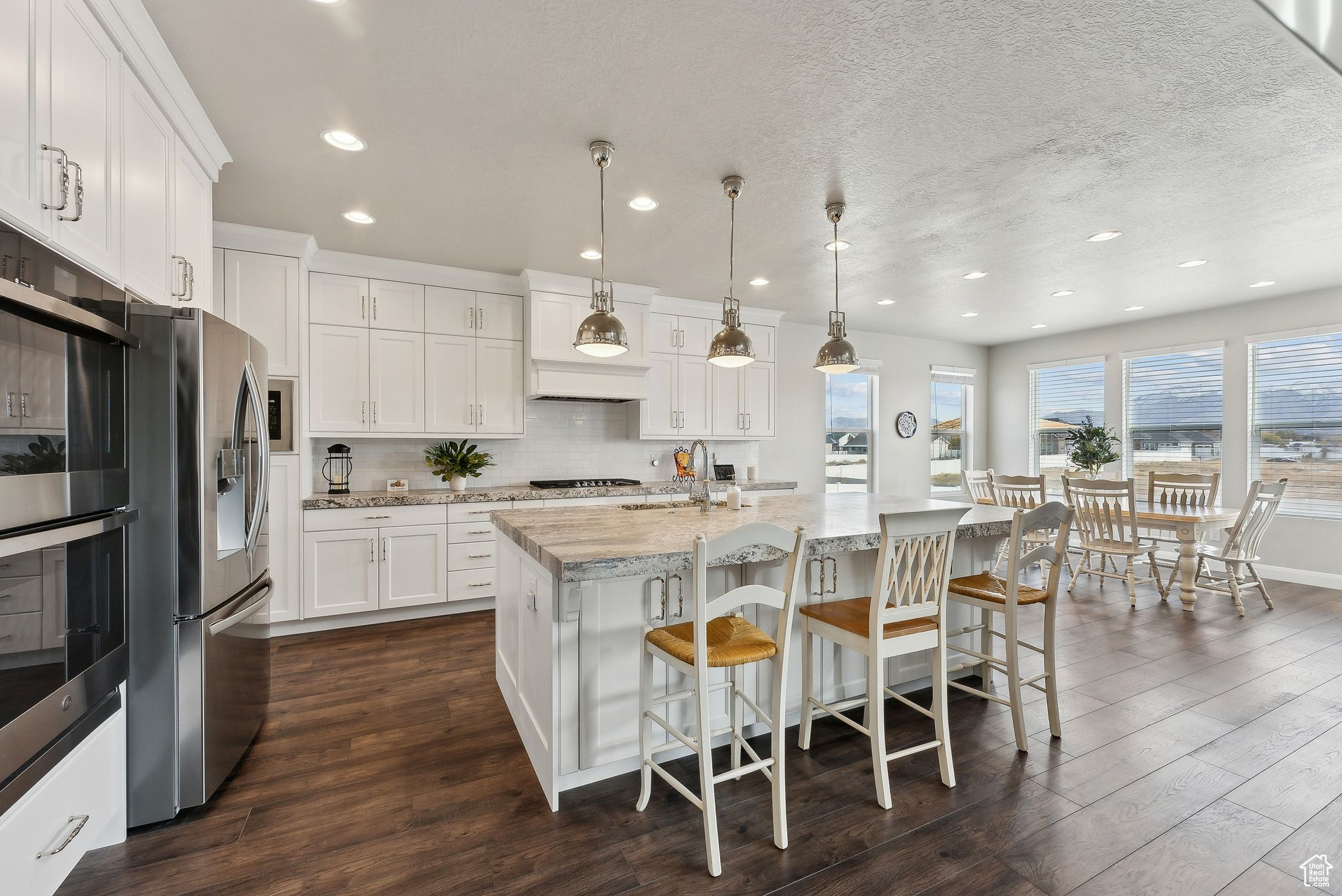 Kitchen featuring white cabinetry, light stone countertops, stainless steel fridge, decorative light fixtures, and a center island with sink