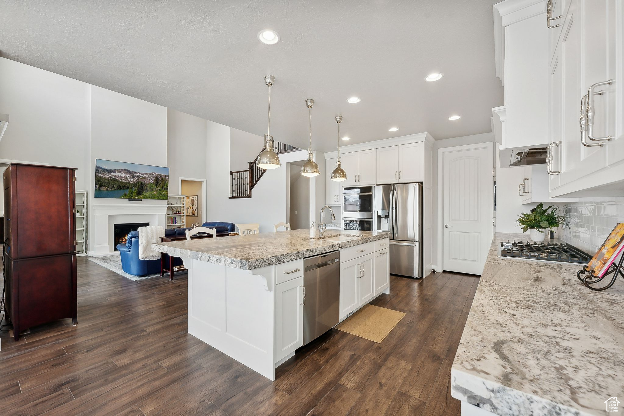 Kitchen featuring a kitchen island with sink, white cabinets, hanging light fixtures, dark hardwood / wood-style flooring, and stainless steel appliances