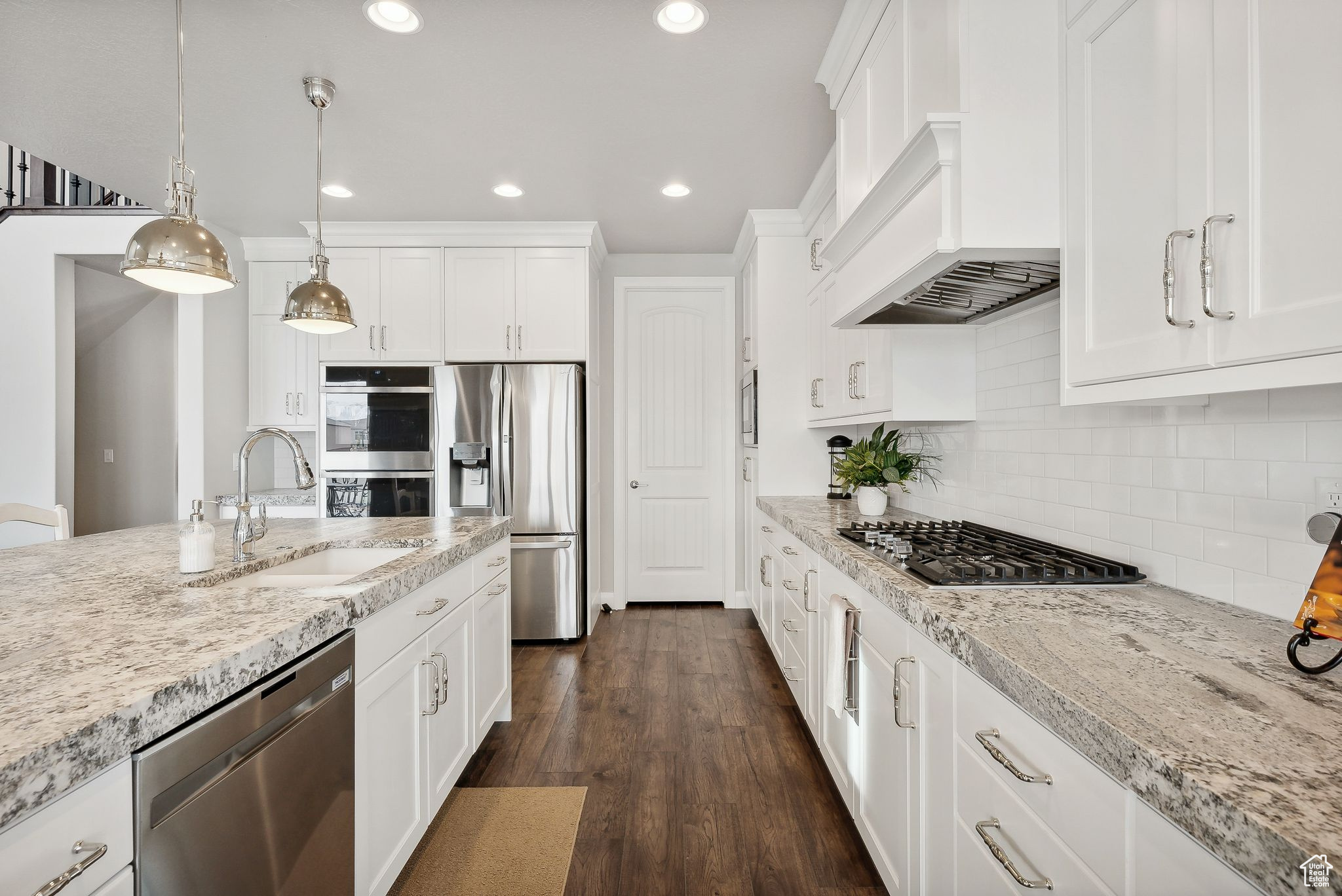 Kitchen with appliances with stainless steel finishes, dark hardwood / wood-style flooring, premium range hood, sink, and hanging light fixtures