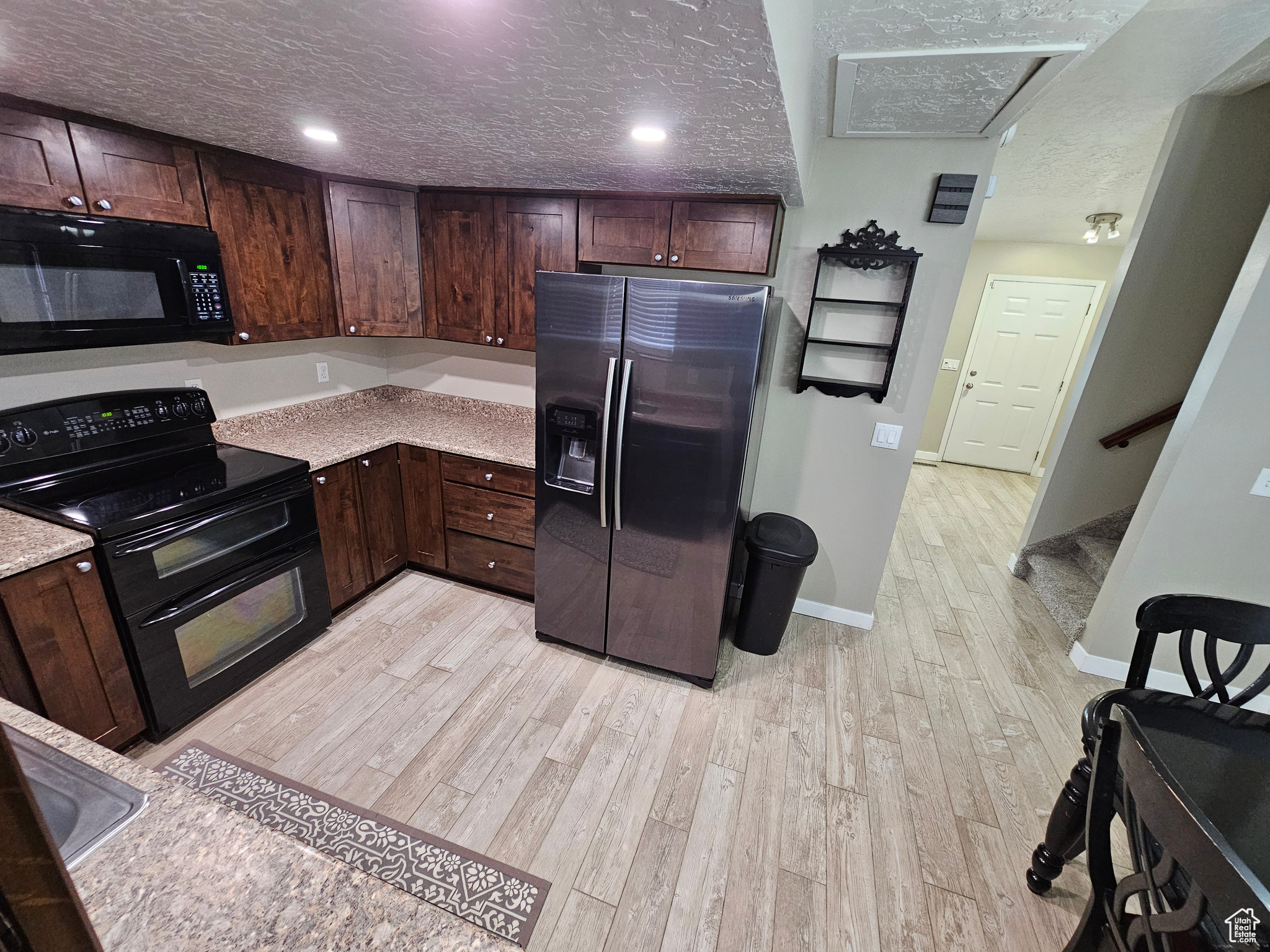 Kitchen featuring black appliances, dark brown cabinets, a textured ceiling, and light hardwood / wood-style flooring