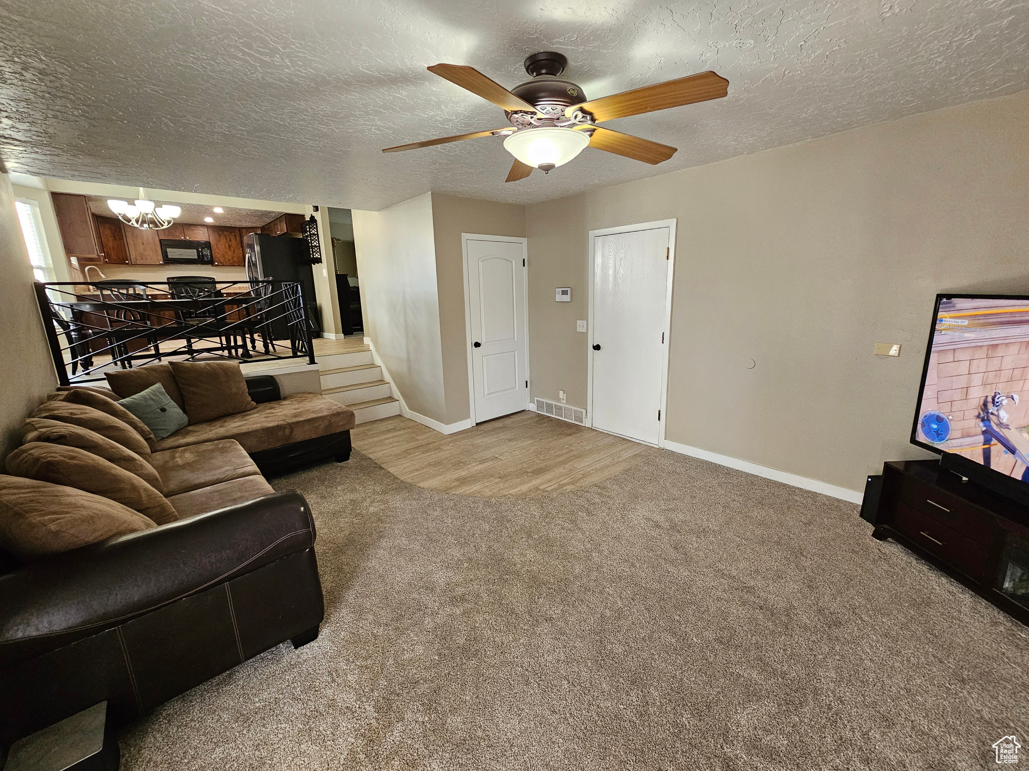 Carpeted living room with ceiling fan with notable chandelier and a textured ceiling