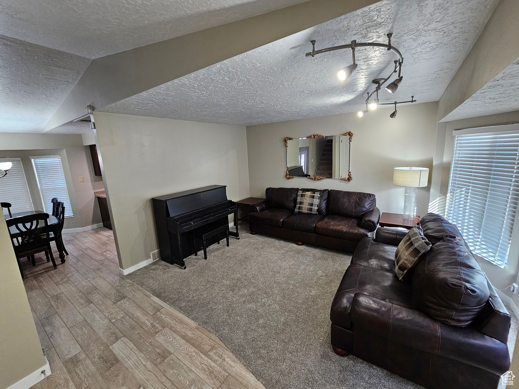 Living room with a textured ceiling, light wood-type flooring, rail lighting, and lofted ceiling