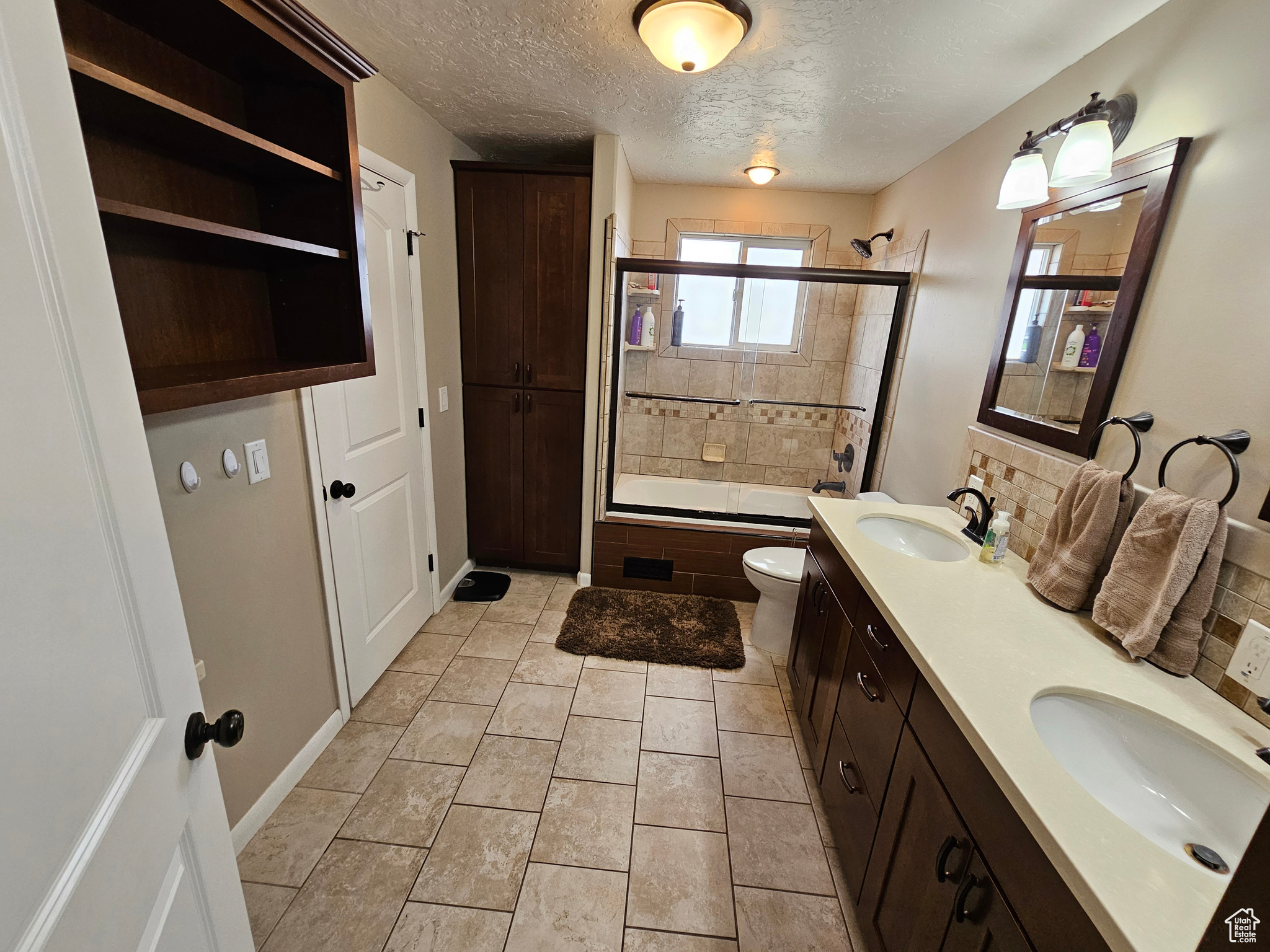 Full bathroom featuring combined bath / shower with glass door, tile patterned flooring, decorative backsplash, toilet, and a textured ceiling