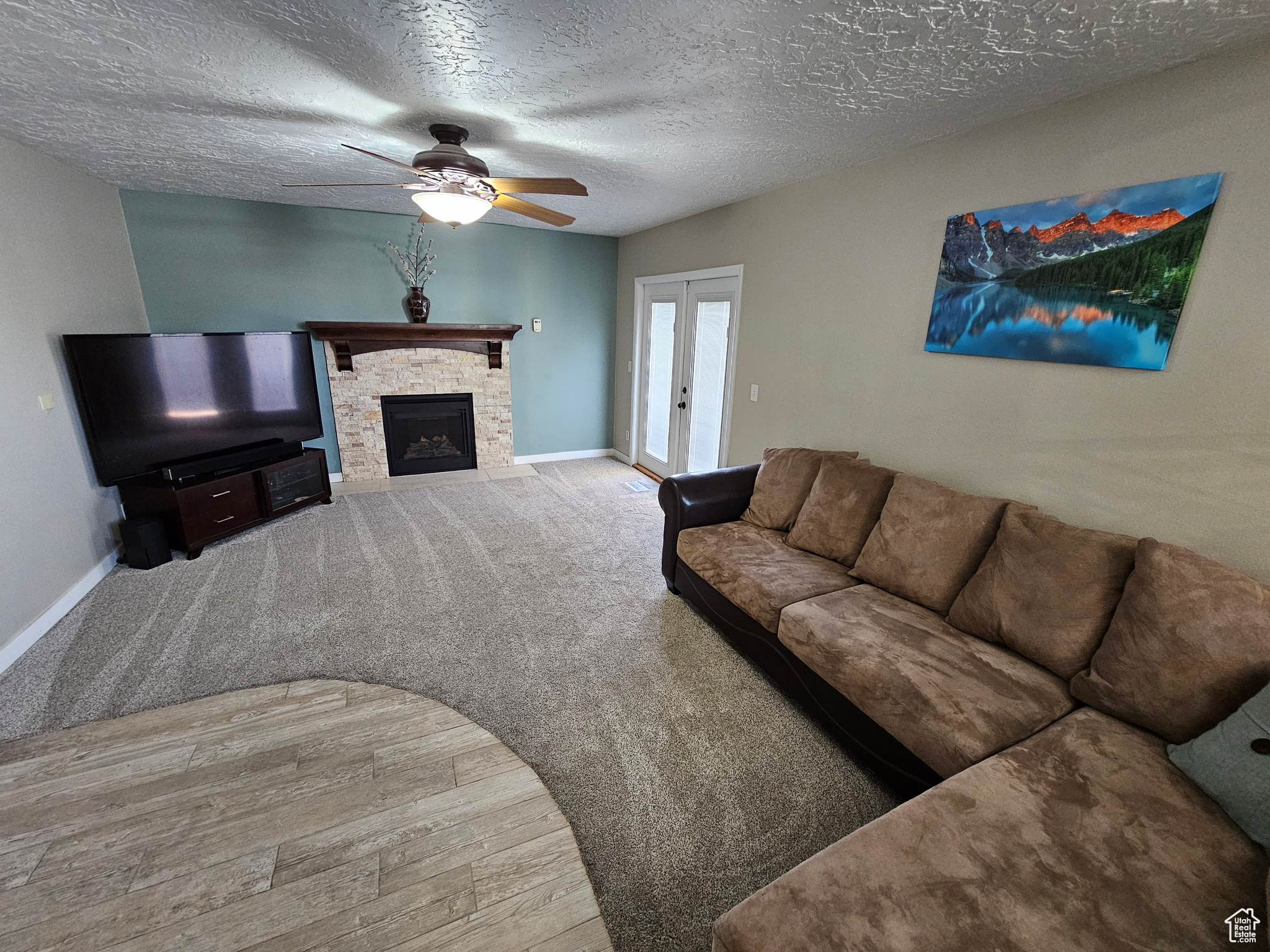 Living room featuring ceiling fan, french doors, hardwood / wood-style floors, a textured ceiling, and a fireplace