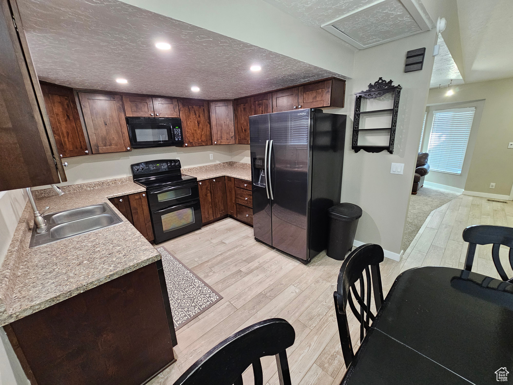 Kitchen with a textured ceiling, sink, light hardwood / wood-style flooring, and black appliances