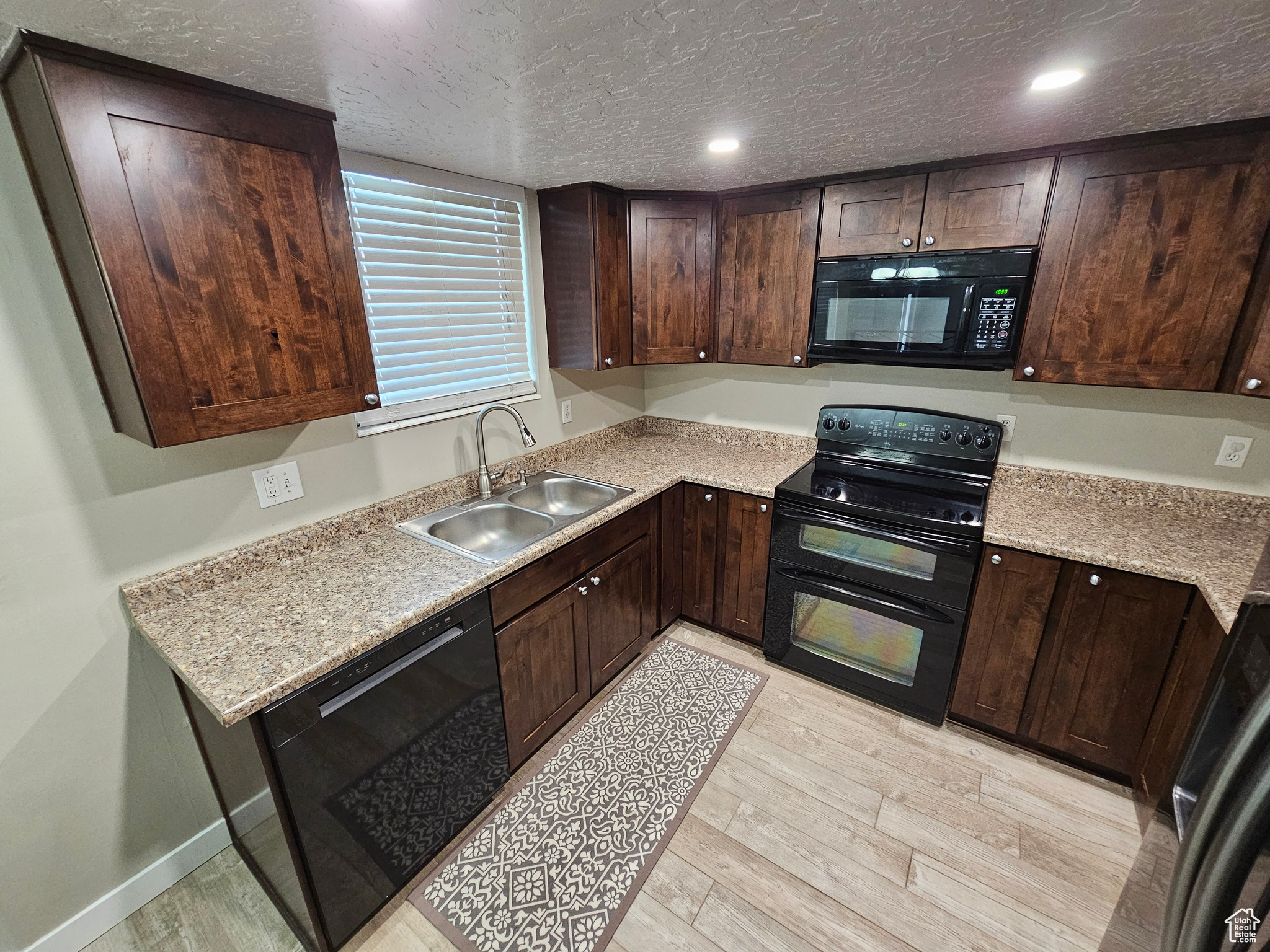 Kitchen featuring light wood-type flooring, sink, dark brown cabinetry, and black appliances