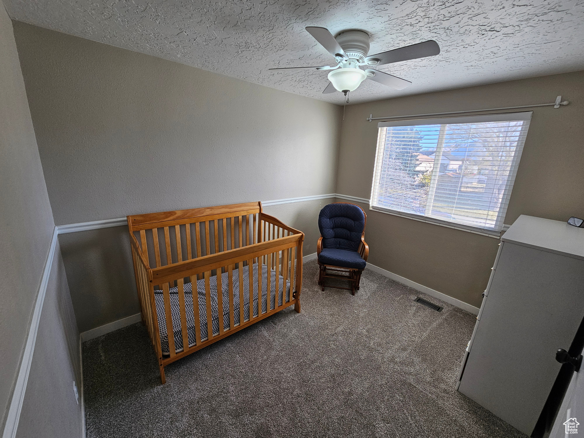 Carpeted bedroom featuring a textured ceiling, a nursery area, and ceiling fan