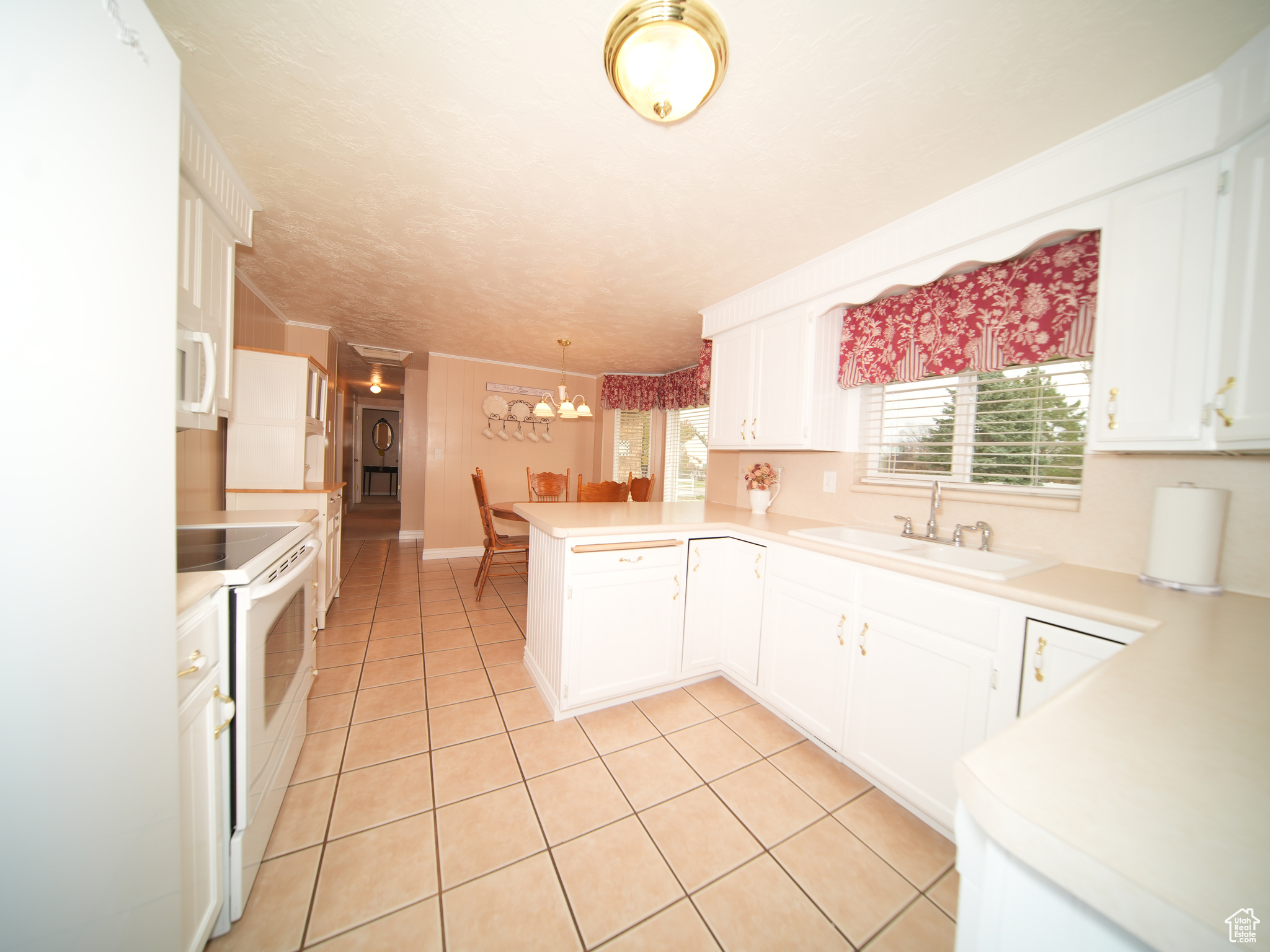 Kitchen with kitchen peninsula, white appliances, white cabinetry, and sink