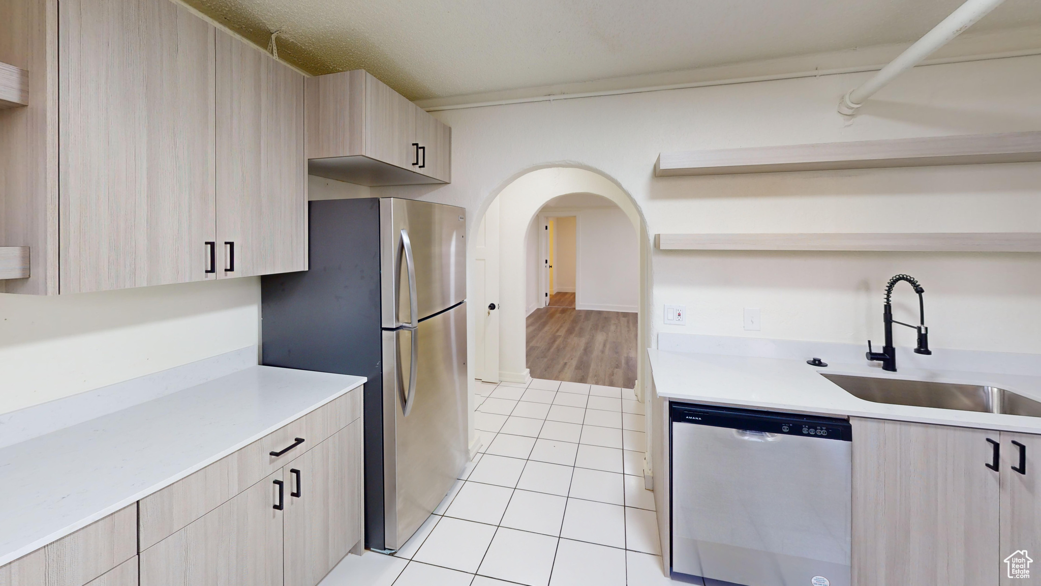 Kitchen with light tile patterned floors, light brown cabinetry, sink, and appliances with stainless steel finishes