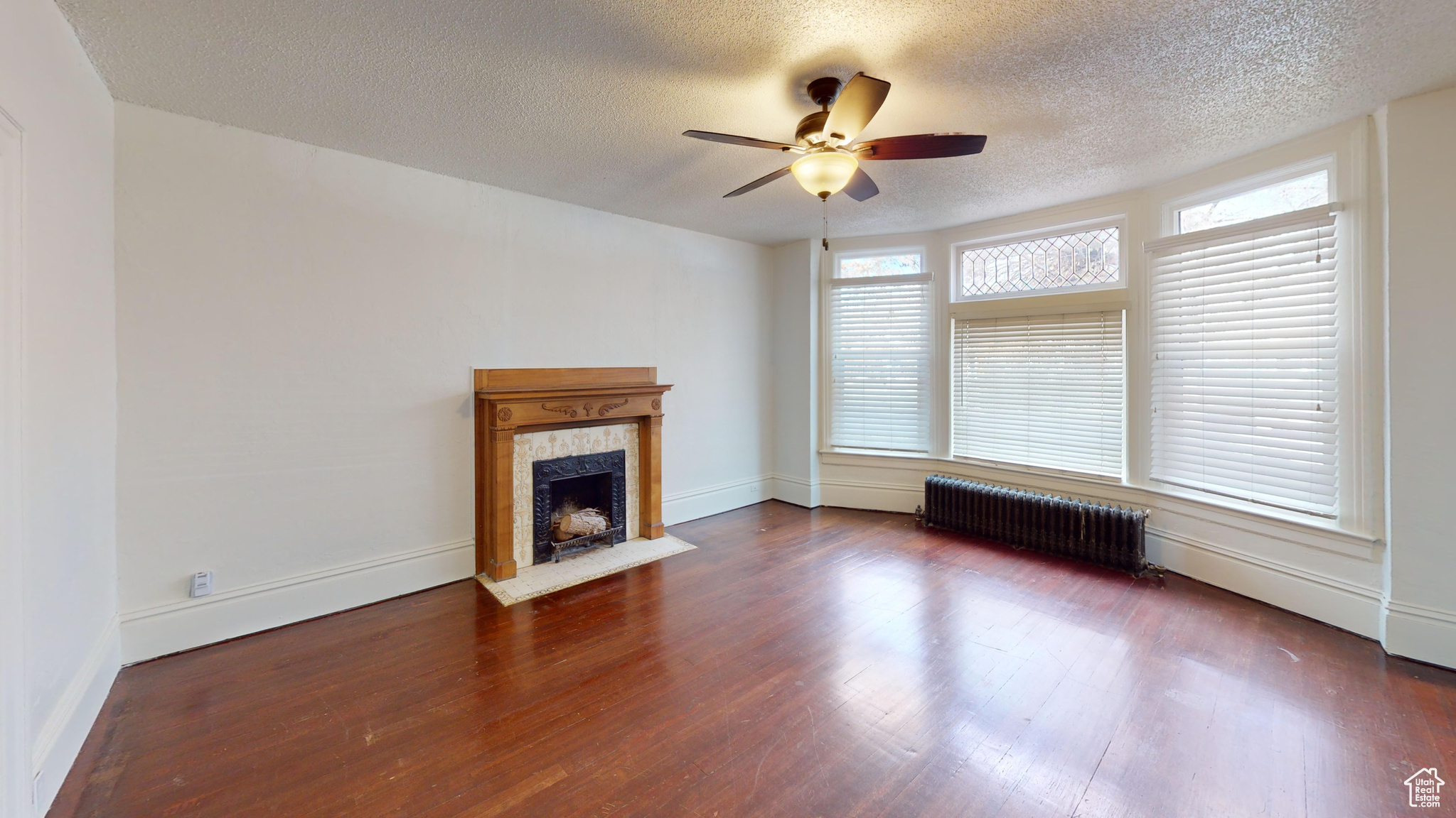 Unfurnished living room with radiator heating unit, dark hardwood / wood-style flooring, a textured ceiling, and a wealth of natural light