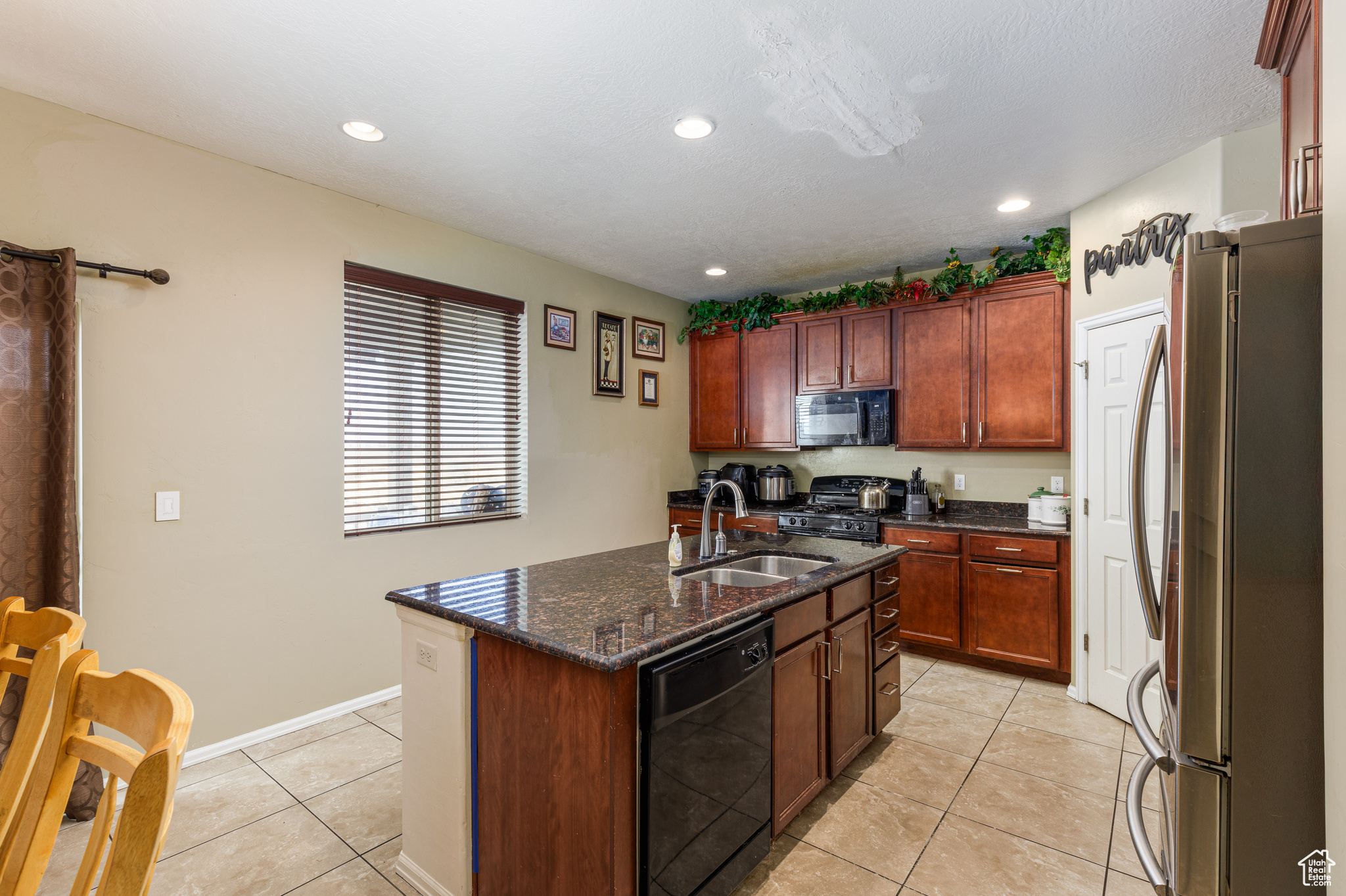 Kitchen with black appliances, sink, dark stone countertops, light tile patterned floors, and an island with sink