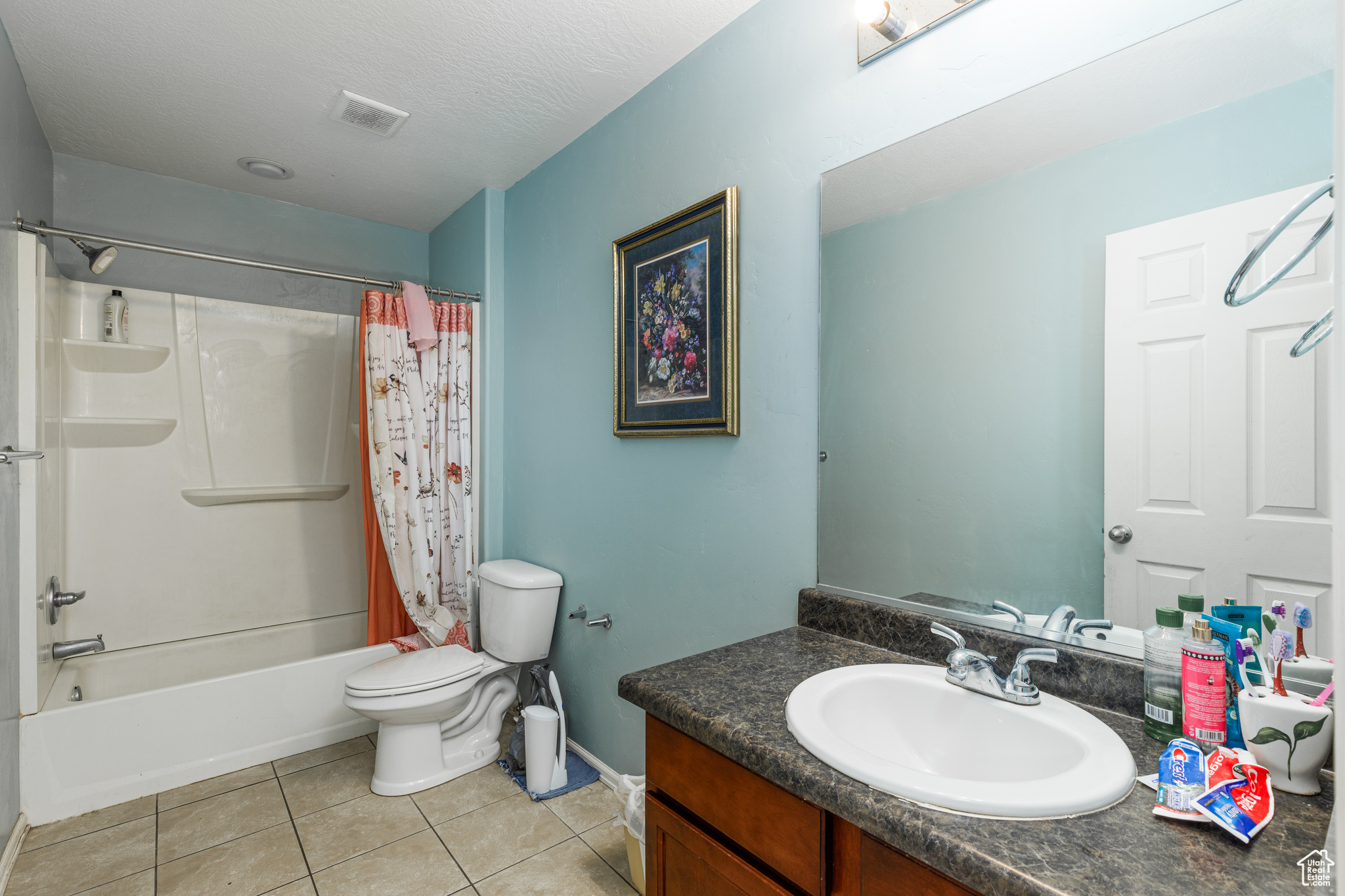 Full bathroom with a textured ceiling, vanity, shower / bathtub combination with curtain, tile patterned flooring, and toilet