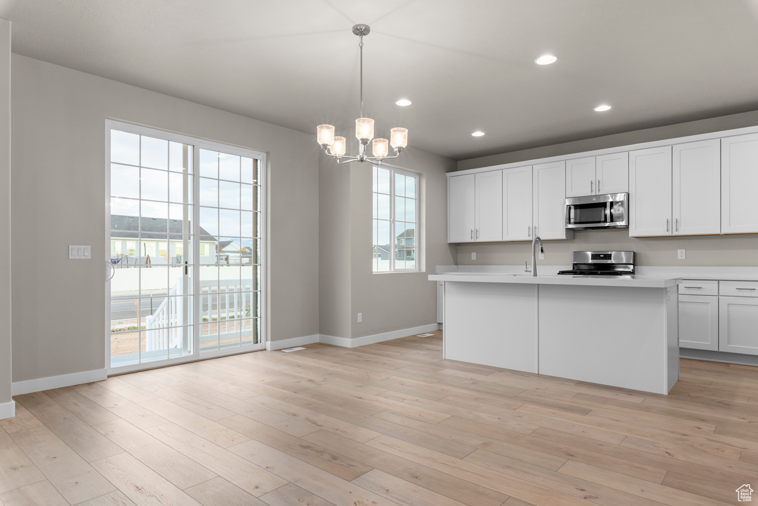 Kitchen with stainless steel appliances, an island with sink, pendant lighting, white cabinets, and light wood-type flooring