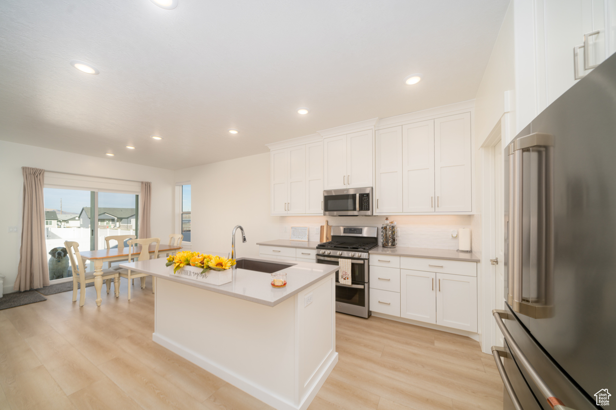 Kitchen featuring white cabinets, stainless steel appliances, a kitchen island with sink, and sink