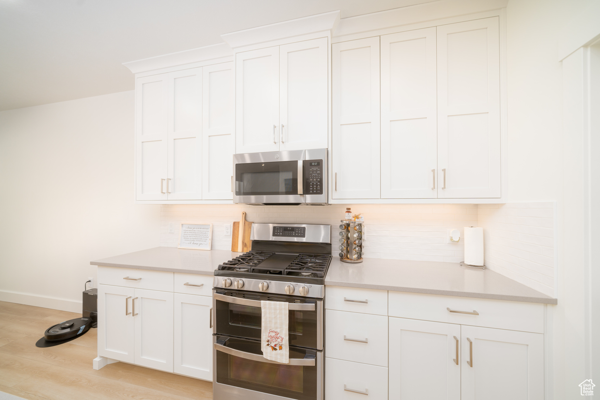 Kitchen with white cabinets, light wood-type flooring, stainless steel appliances, and tasteful backsplash