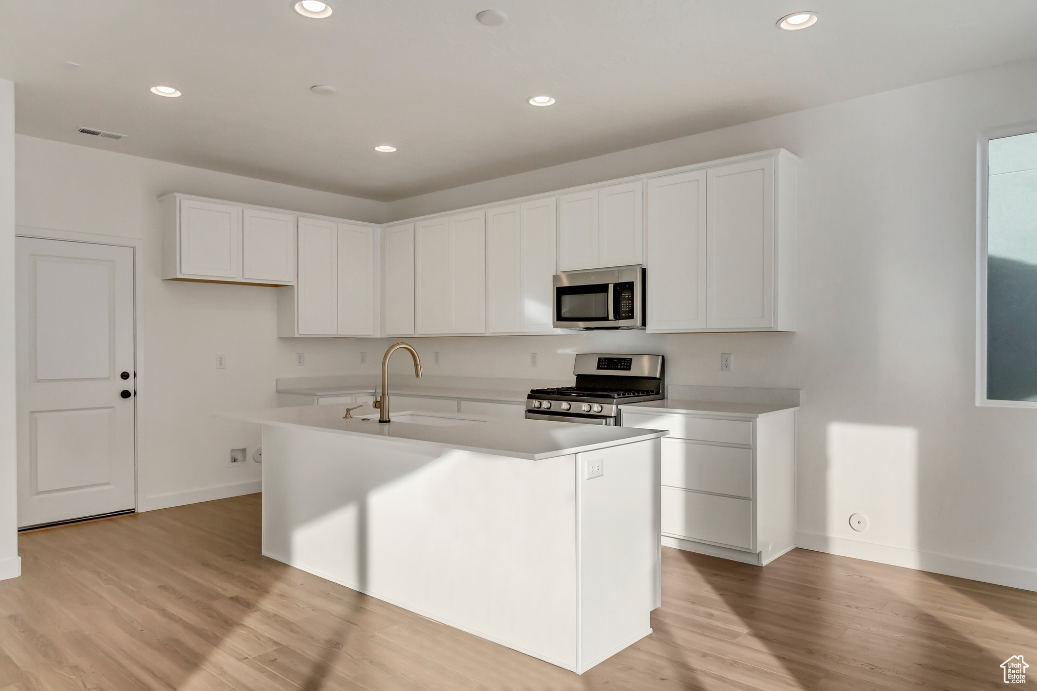 Kitchen featuring white cabinets, sink, light hardwood / wood-style flooring, an island with sink, and appliances with stainless steel finishes