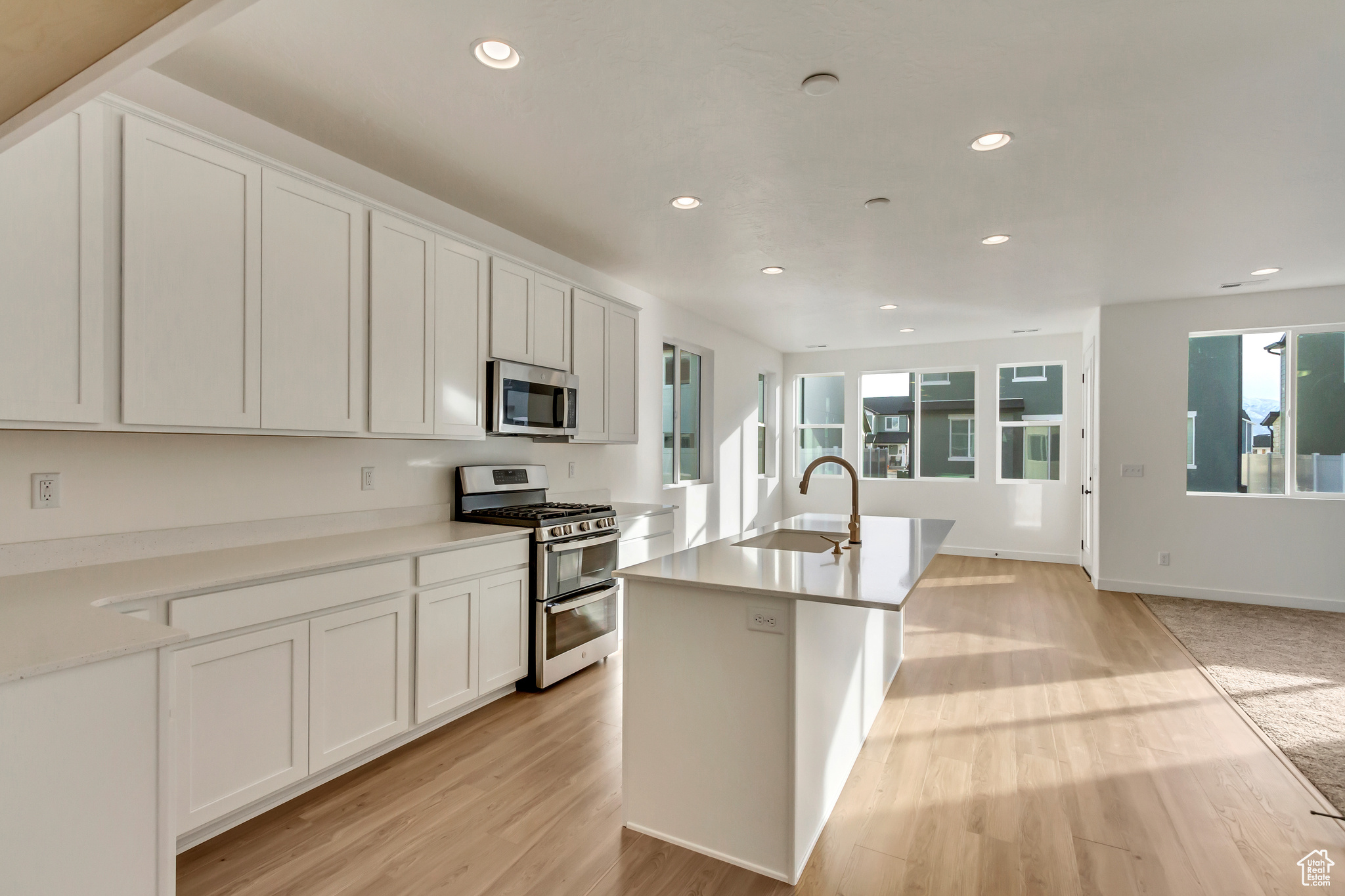 Kitchen with sink, light wood-type flooring, an island with sink, appliances with stainless steel finishes, and white cabinetry