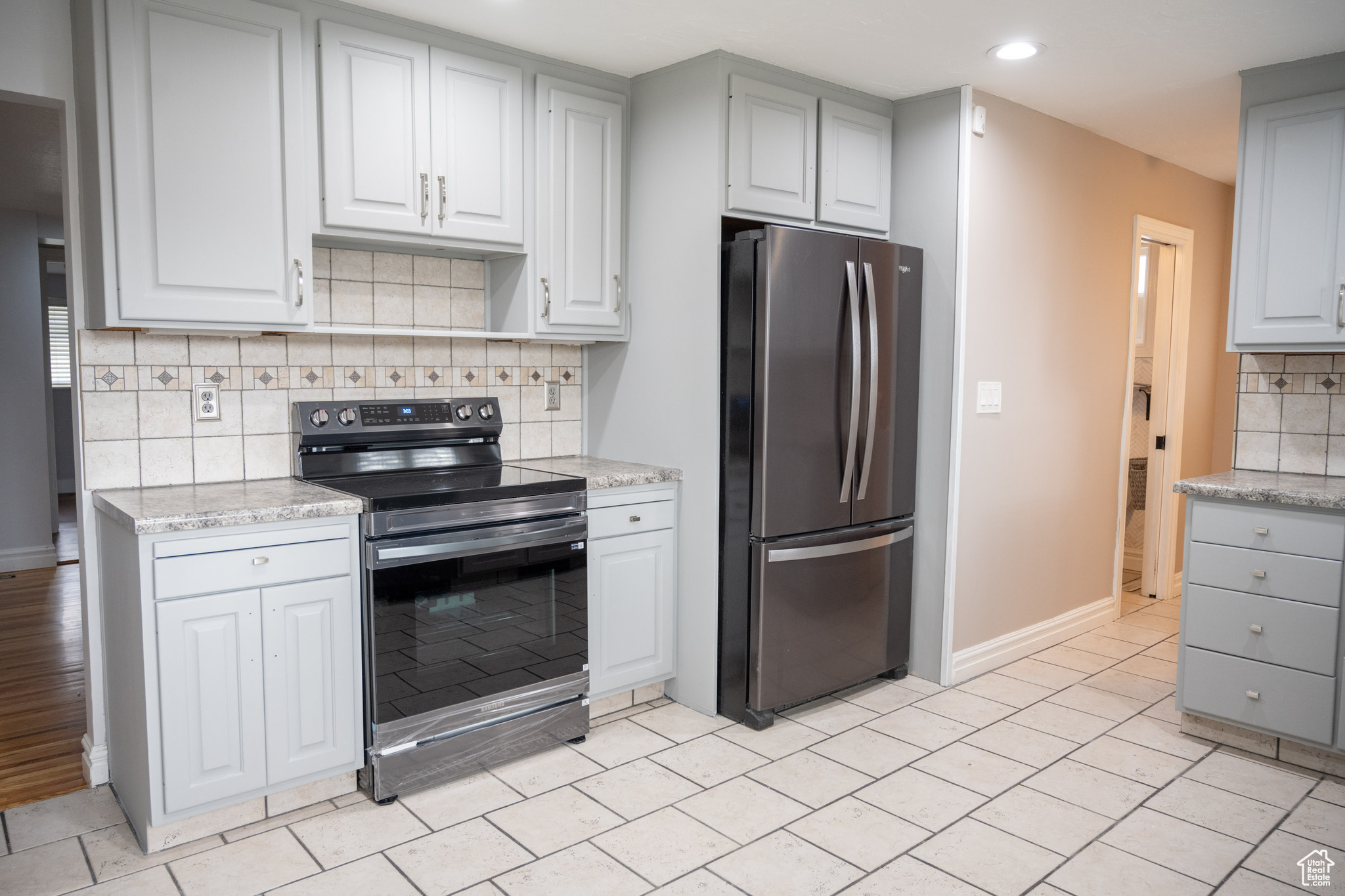 Kitchen with tasteful backsplash, stainless steel refrigerator, light stone countertops, and black / electric stove