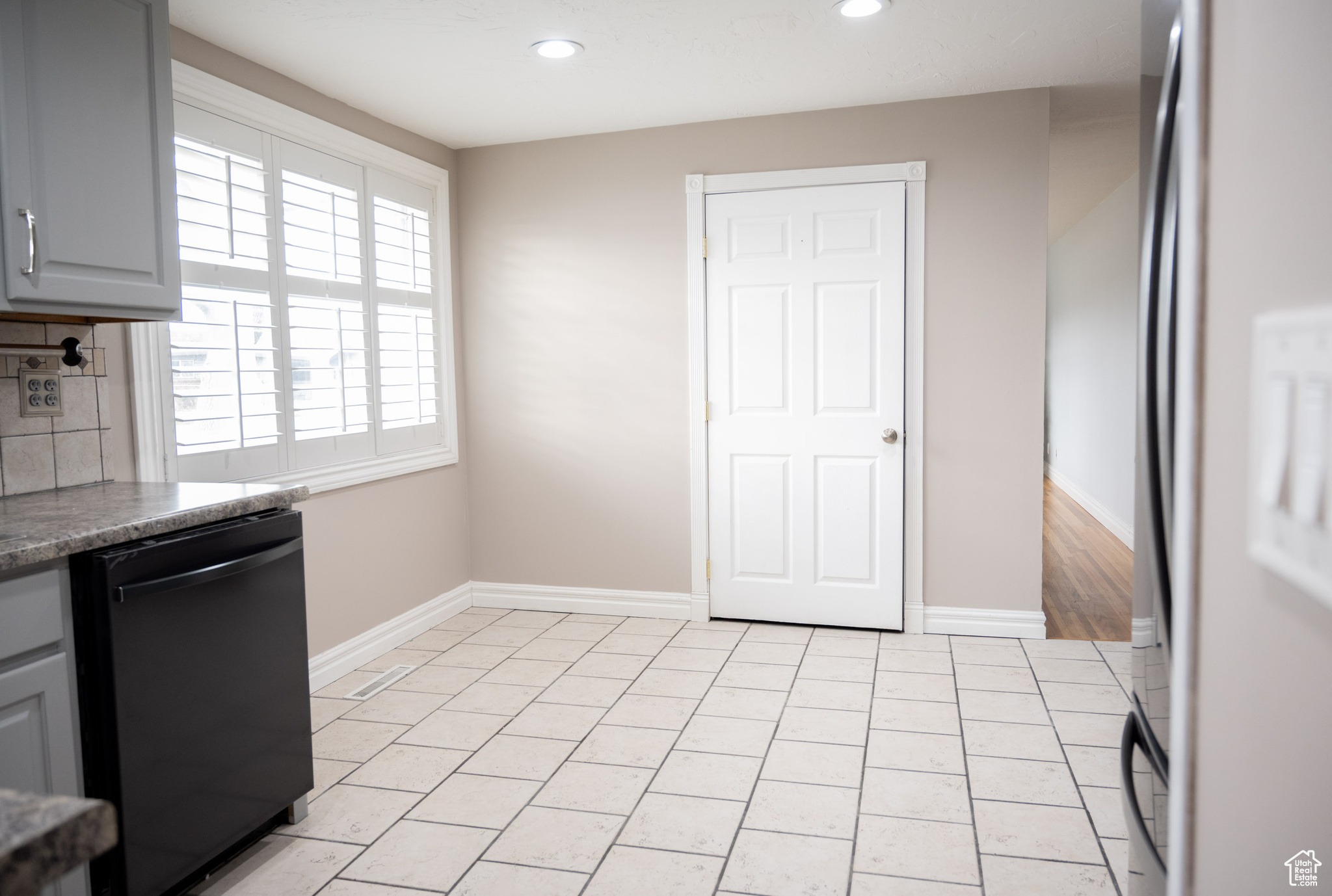 Kitchen featuring gray cabinetry, decorative backsplash, light tile patterned floors, black dishwasher, and stainless steel refrigerator