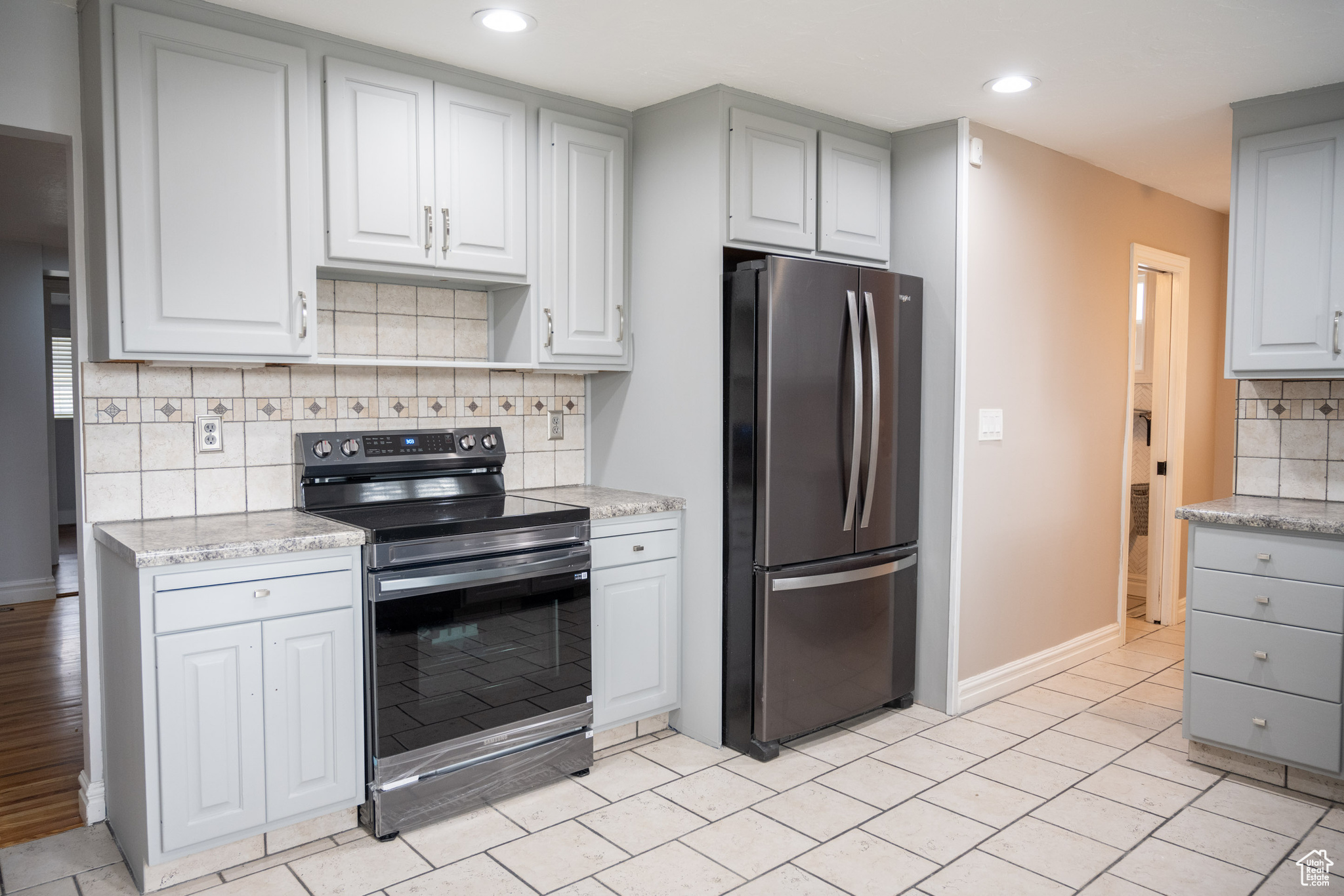 Kitchen featuring decorative backsplash, black electric range oven, light stone counters, and stainless steel refrigerator