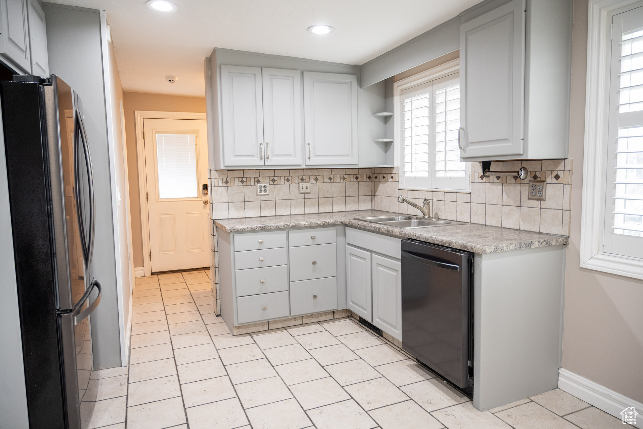 Kitchen featuring stainless steel fridge, backsplash, sink, light tile patterned floors, and black dishwasher