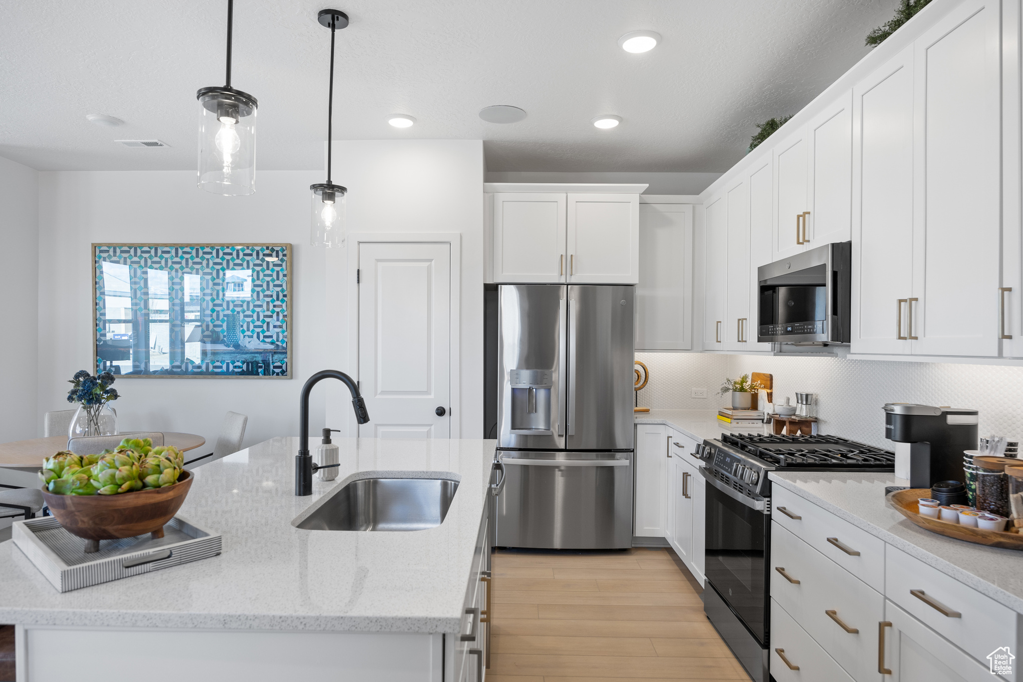 Kitchen featuring sink, hanging light fixtures, a kitchen island with sink, appliances with stainless steel finishes, and light wood-type flooring