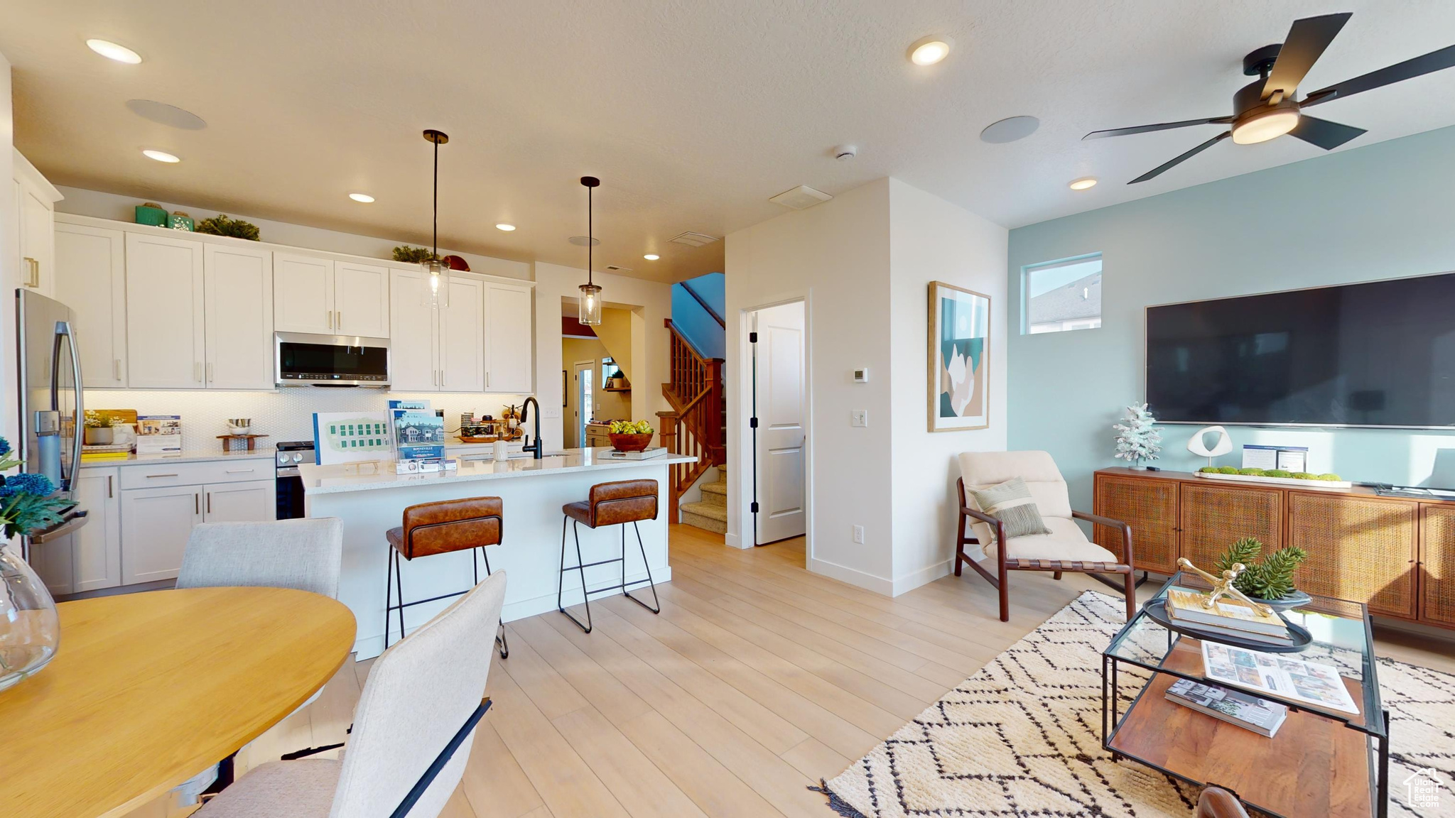 Kitchen featuring appliances with stainless steel finishes, decorative light fixtures, a center island with sink, white cabinets, and light wood-type flooring