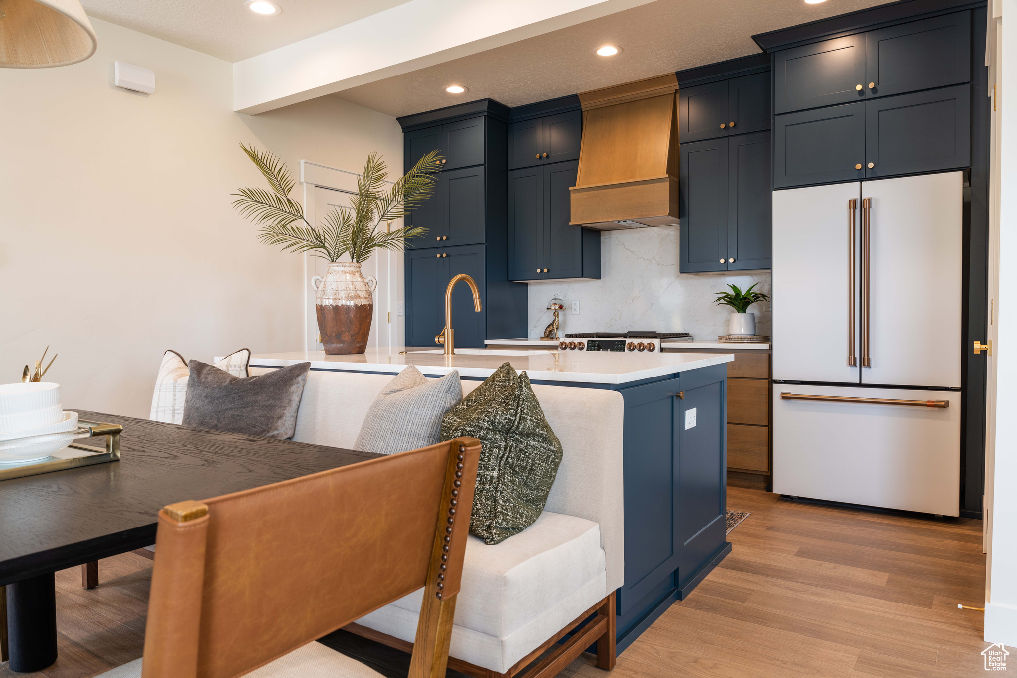 Kitchen with light hardwood / wood-style flooring, high end white refrigerator, decorative backsplash, a center island with sink, and custom exhaust hood