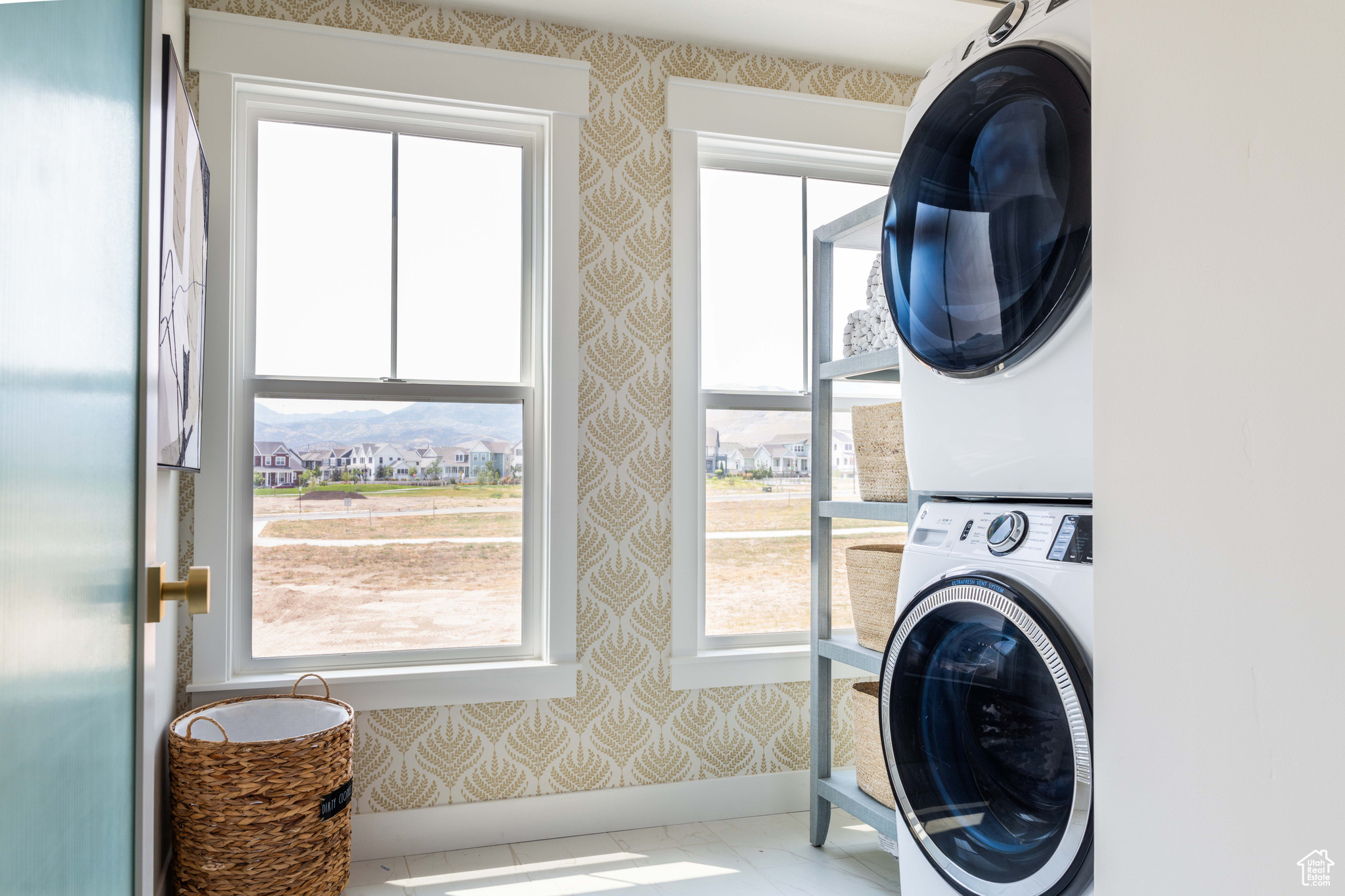 Clothes washing area featuring tile patterned flooring, a healthy amount of sunlight, and stacked washer / drying machine