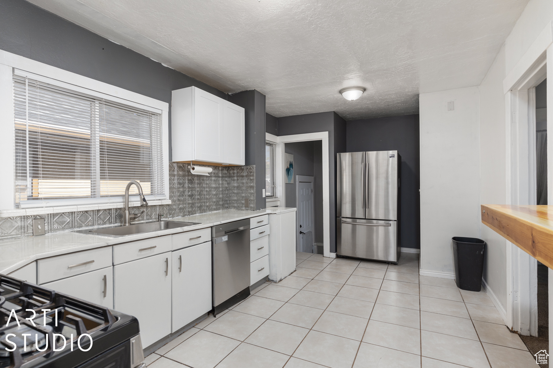 Kitchen featuring backsplash, stainless steel appliances, sink, light tile patterned floors, and white cabinets