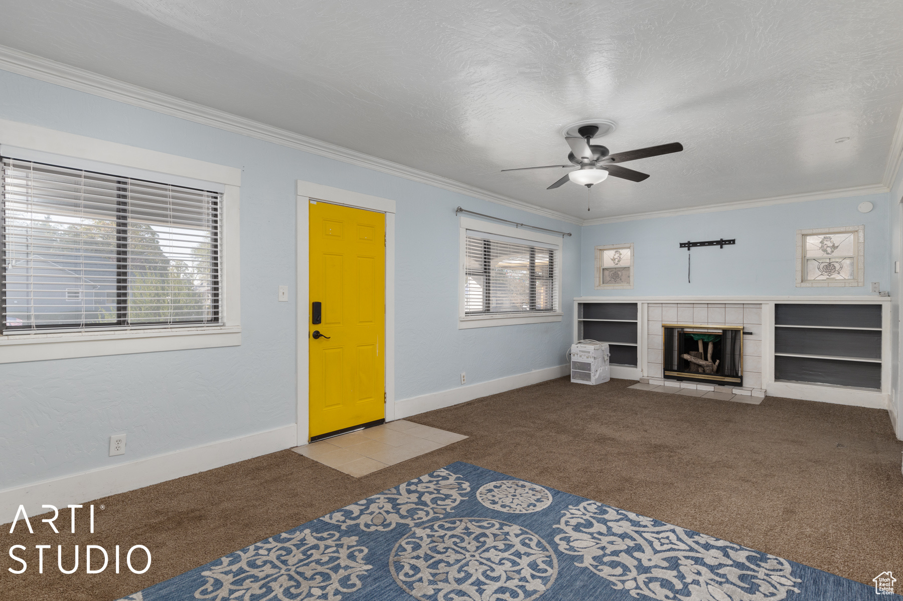 Unfurnished living room featuring a tiled fireplace, ceiling fan, carpet, and ornamental molding