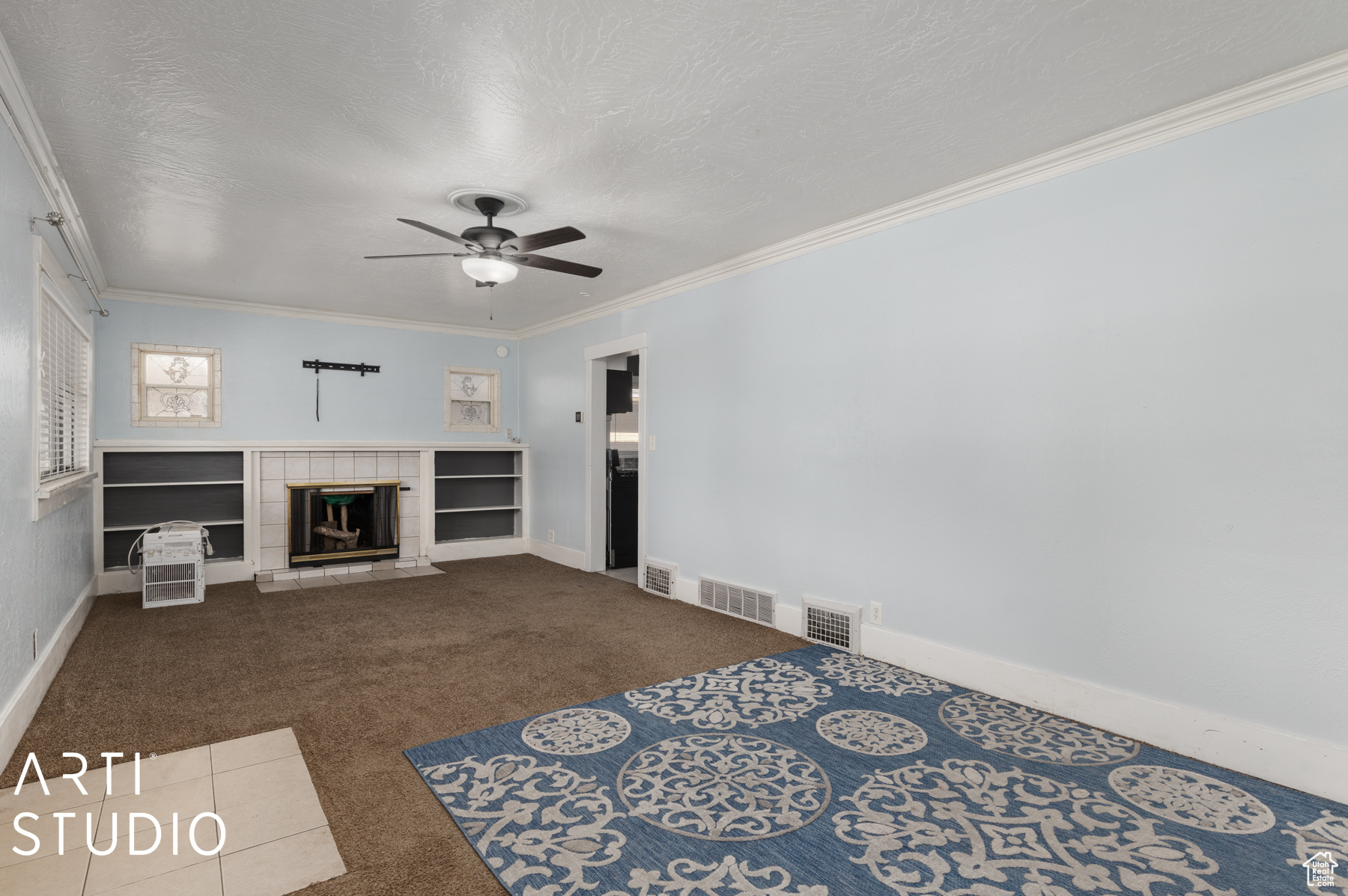 Unfurnished living room with a tile fireplace, crown molding, carpet flooring, ceiling fan, and a textured ceiling