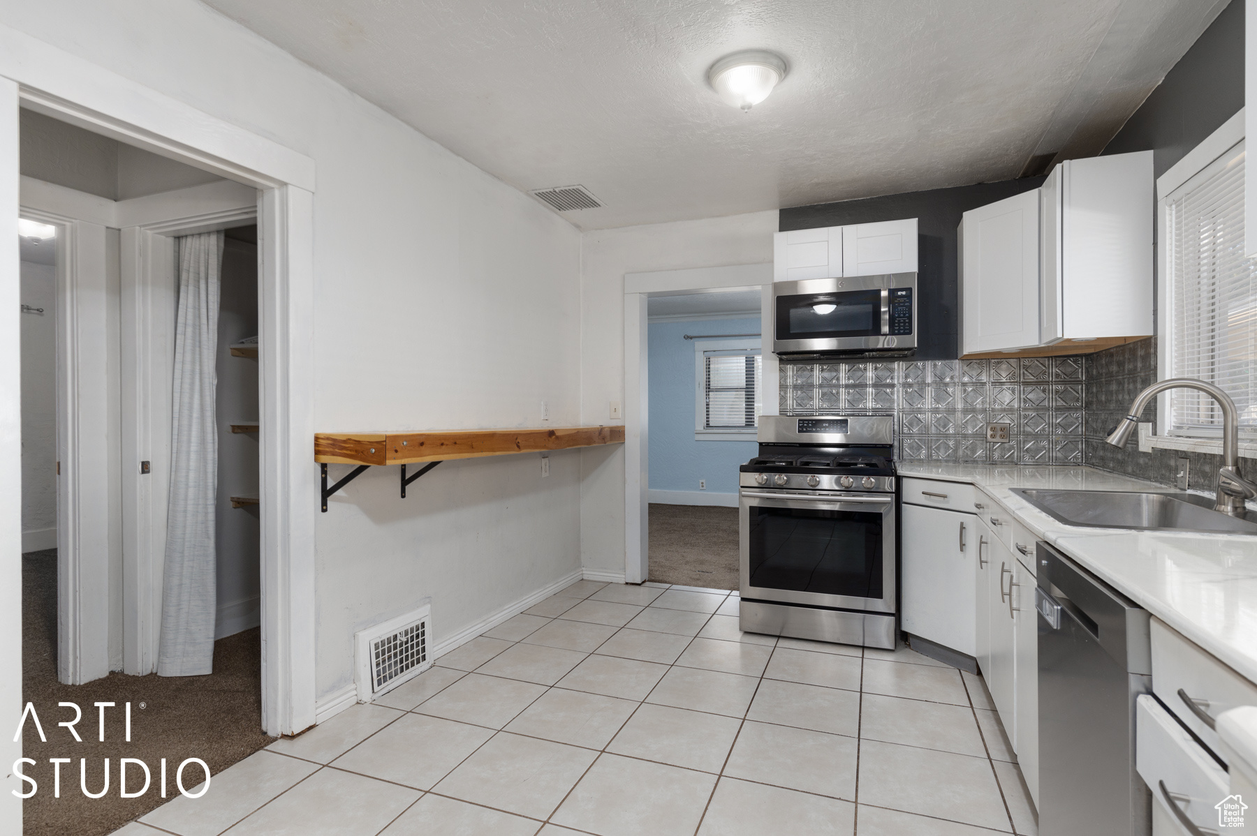 Kitchen with decorative backsplash, appliances with stainless steel finishes, sink, white cabinets, and light tile patterned flooring