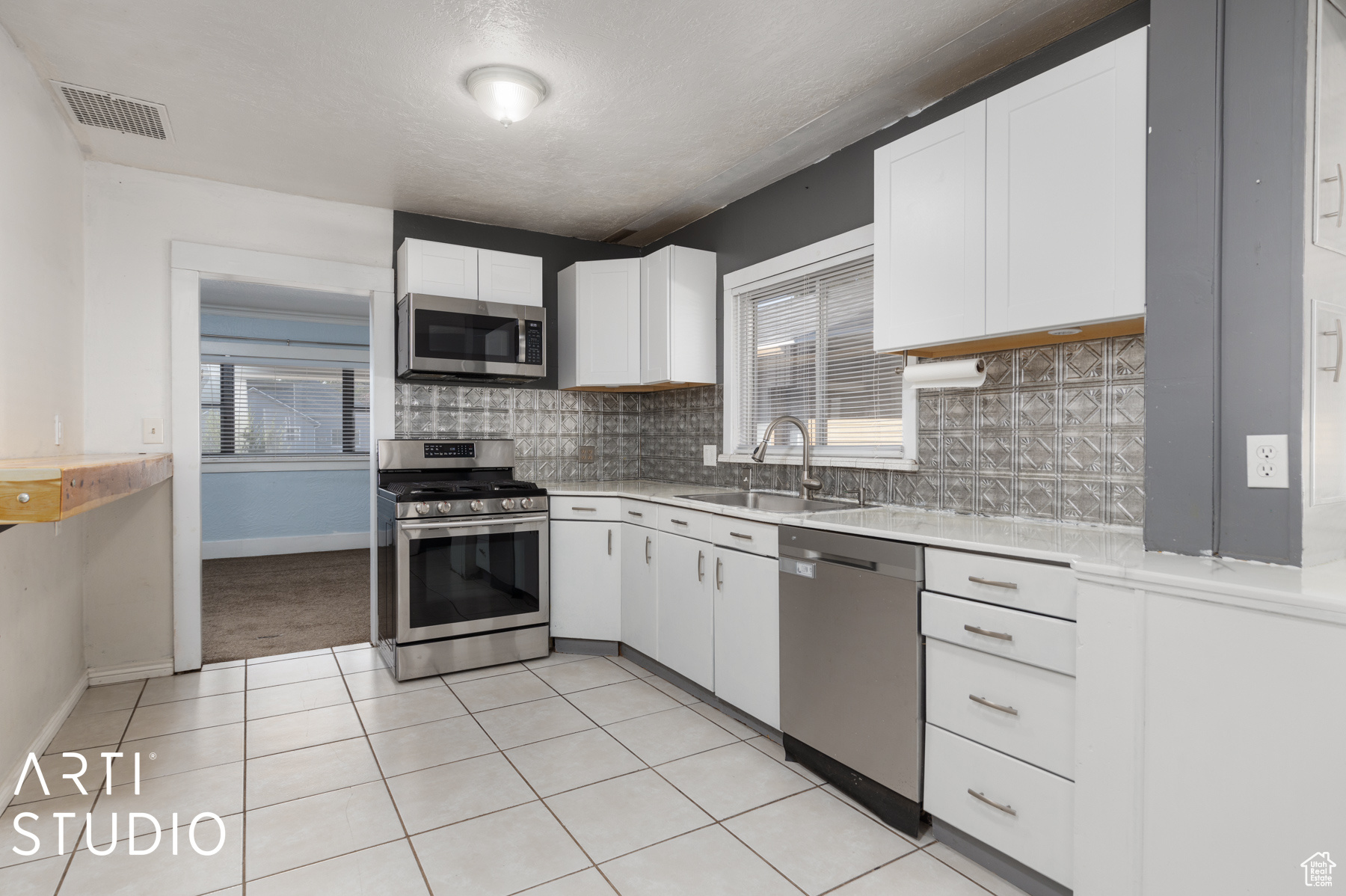 Kitchen with decorative backsplash, white cabinetry, sink, and stainless steel appliances