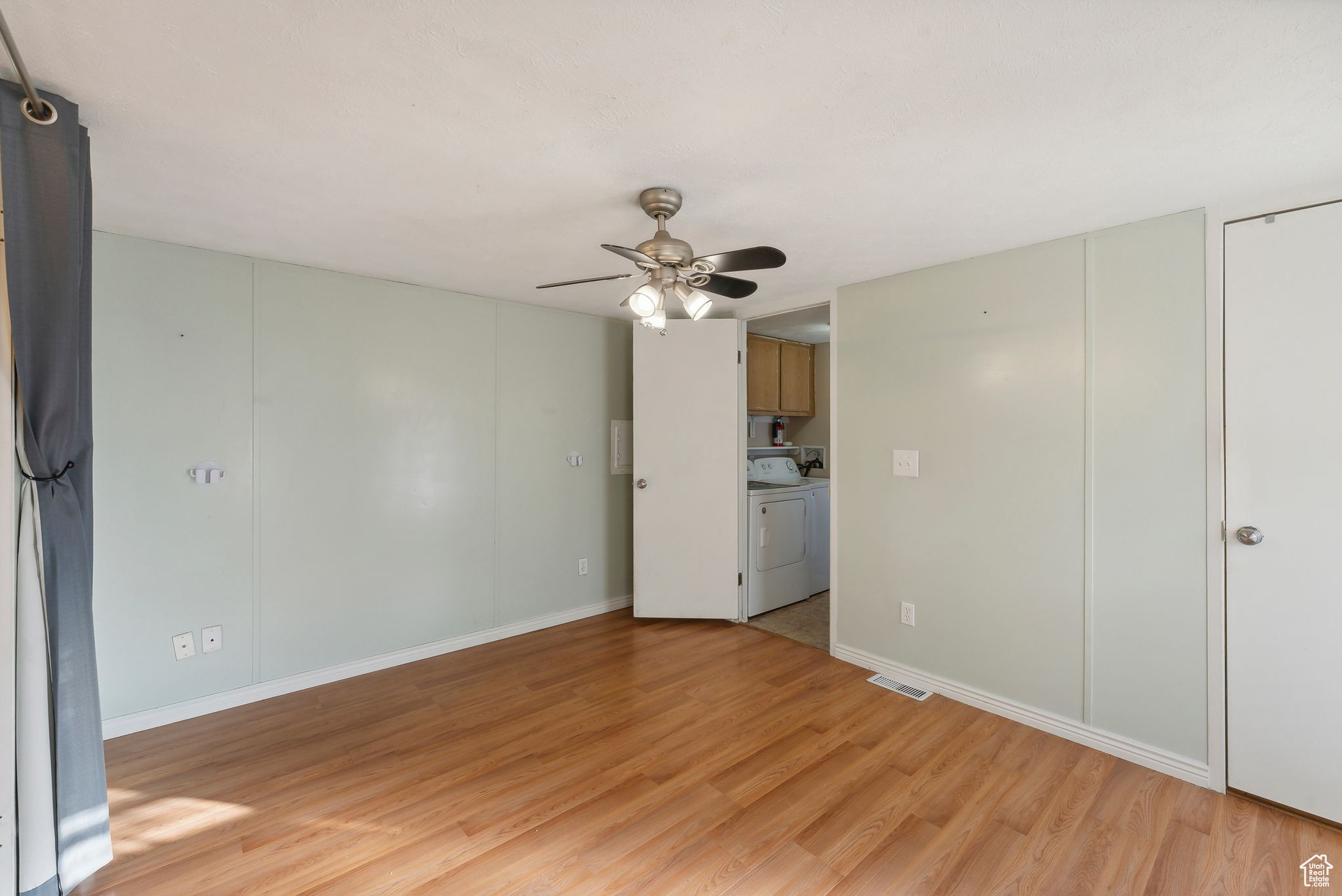 Spare room featuring independent washer and dryer, light wood-type flooring, and ceiling fan