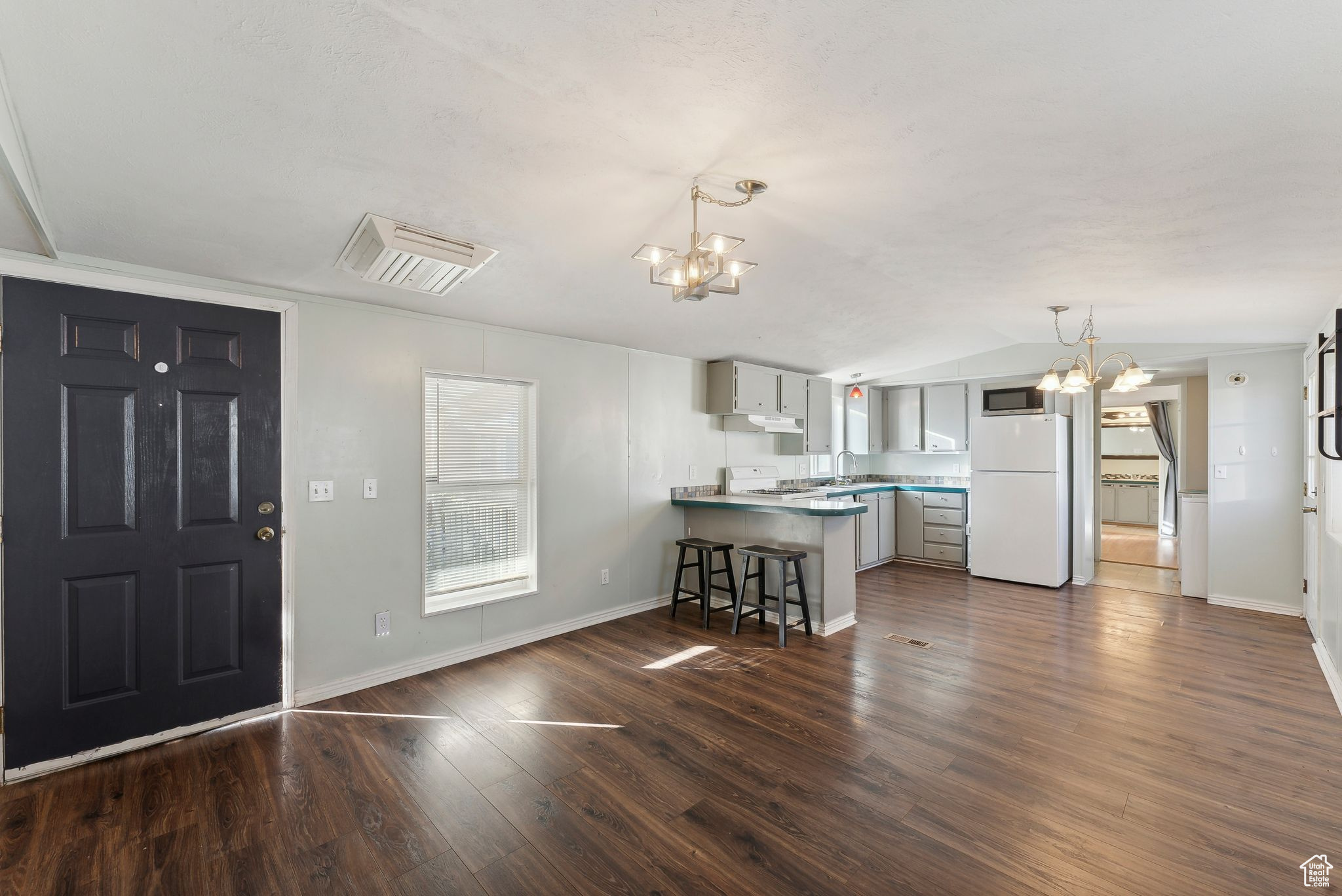 Kitchen featuring white appliances, dark hardwood / wood-style floors, kitchen peninsula, a breakfast bar area, and a chandelier