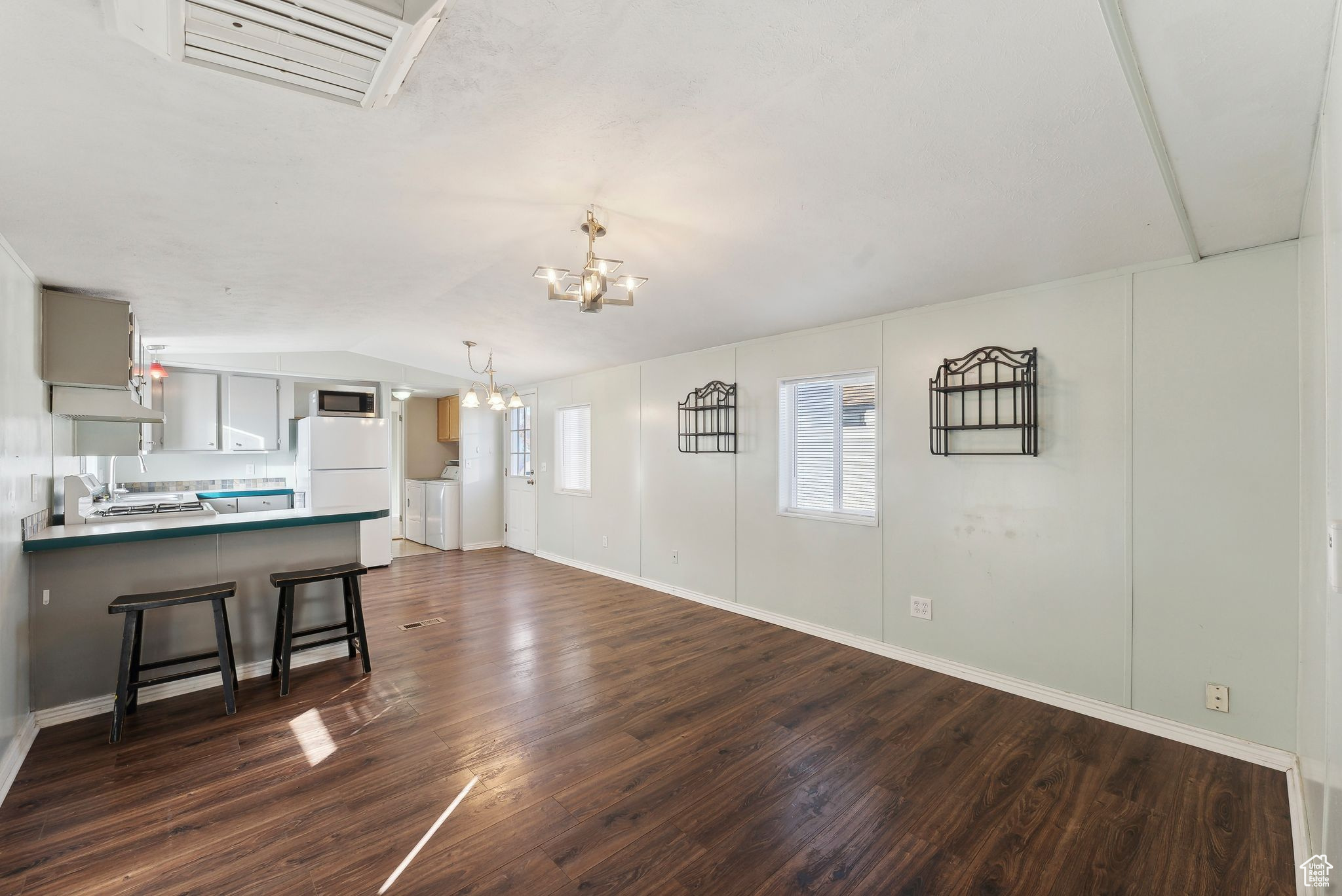 Unfurnished living room with an inviting chandelier, dark hardwood / wood-style floors, vaulted ceiling, and washer and clothes dryer