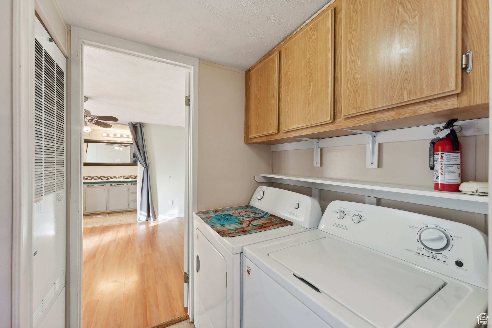 Washroom with cabinets, washer and dryer, ceiling fan, light wood-type flooring, and a textured ceiling