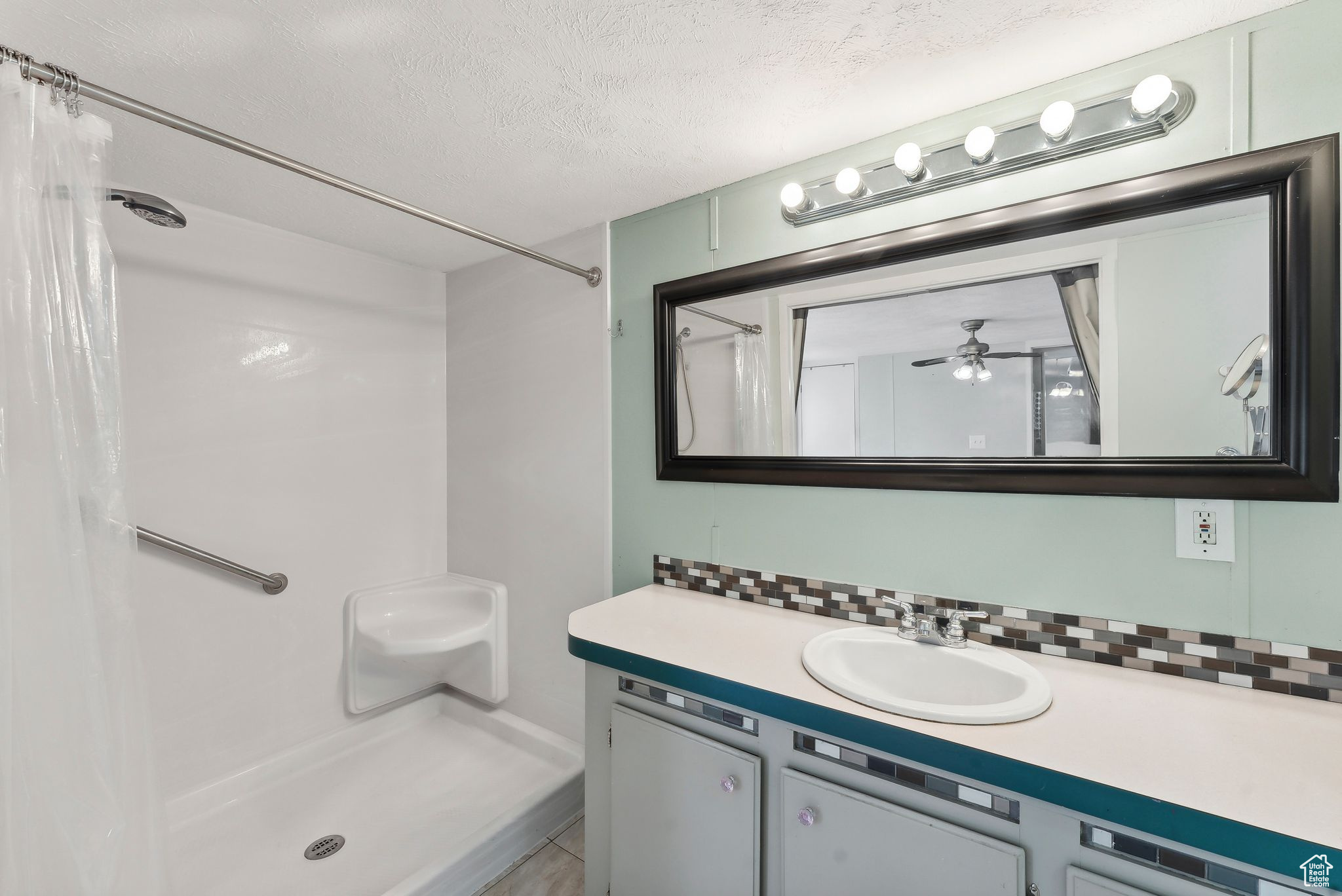 Bathroom with ceiling fan, vanity, a textured ceiling, and walk in shower