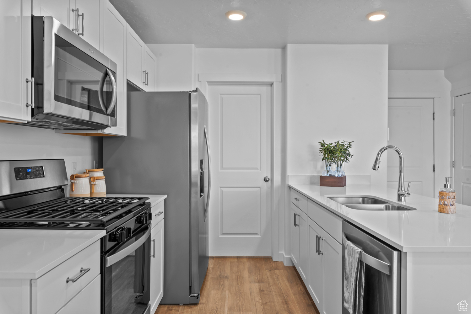 Kitchen with light wood-type flooring, stainless steel appliances, white cabinetry, and sink