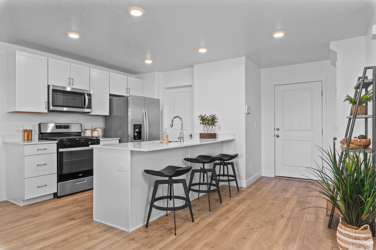 Kitchen featuring white cabinets, light wood-type flooring, appliances with stainless steel finishes, a kitchen bar, and kitchen peninsula