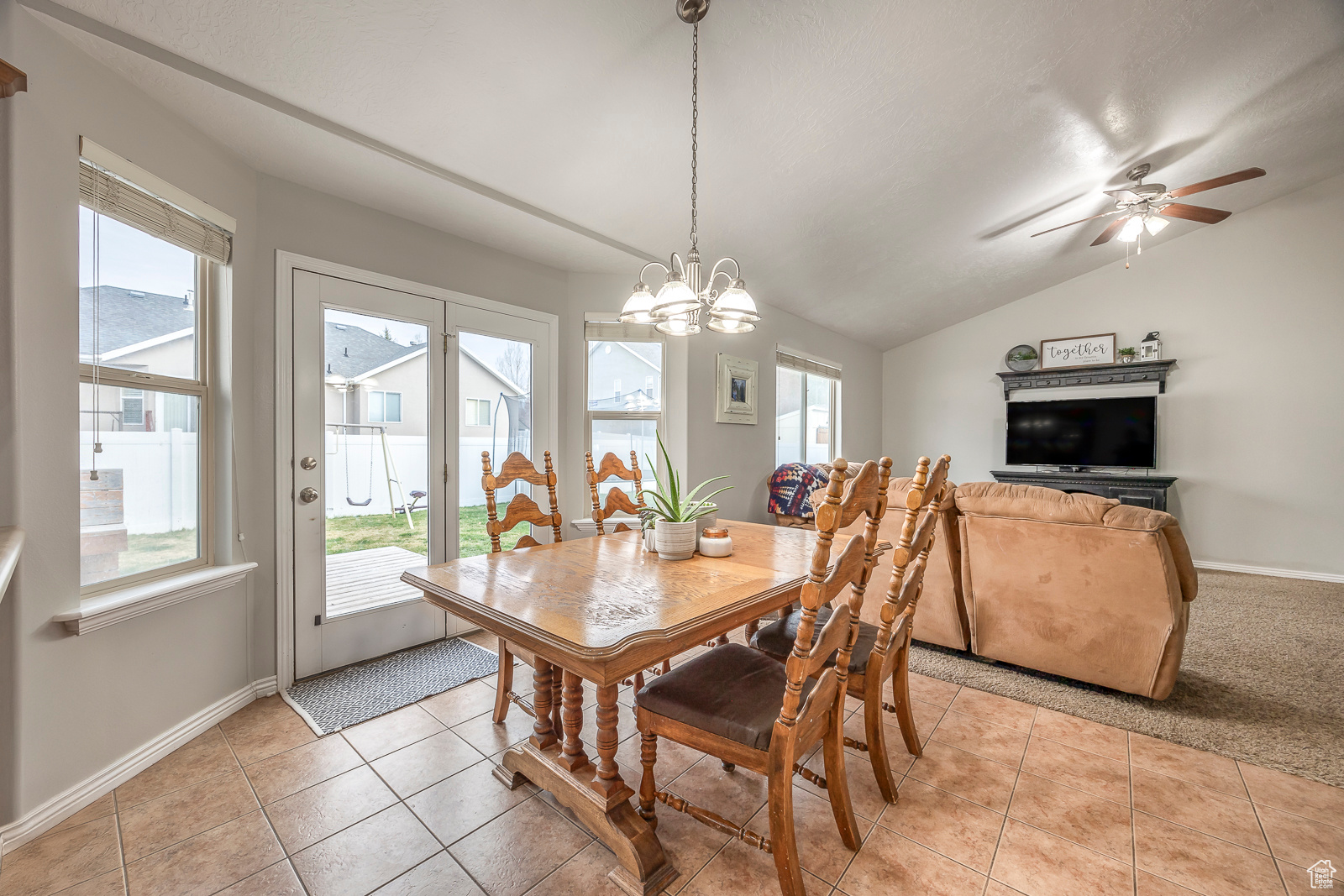 Dining room featuring ceiling fan with notable chandelier, vaulted ceiling, and light tile patterned flooring