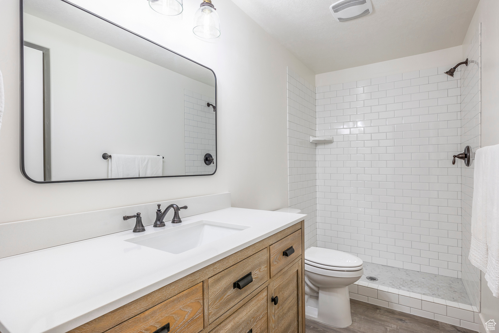 Bathroom with hardwood / wood-style floors, vanity, a tile shower, and toilet