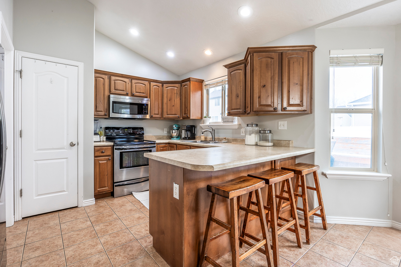 Kitchen featuring sink, stainless steel appliances, kitchen peninsula, vaulted ceiling, and a breakfast bar