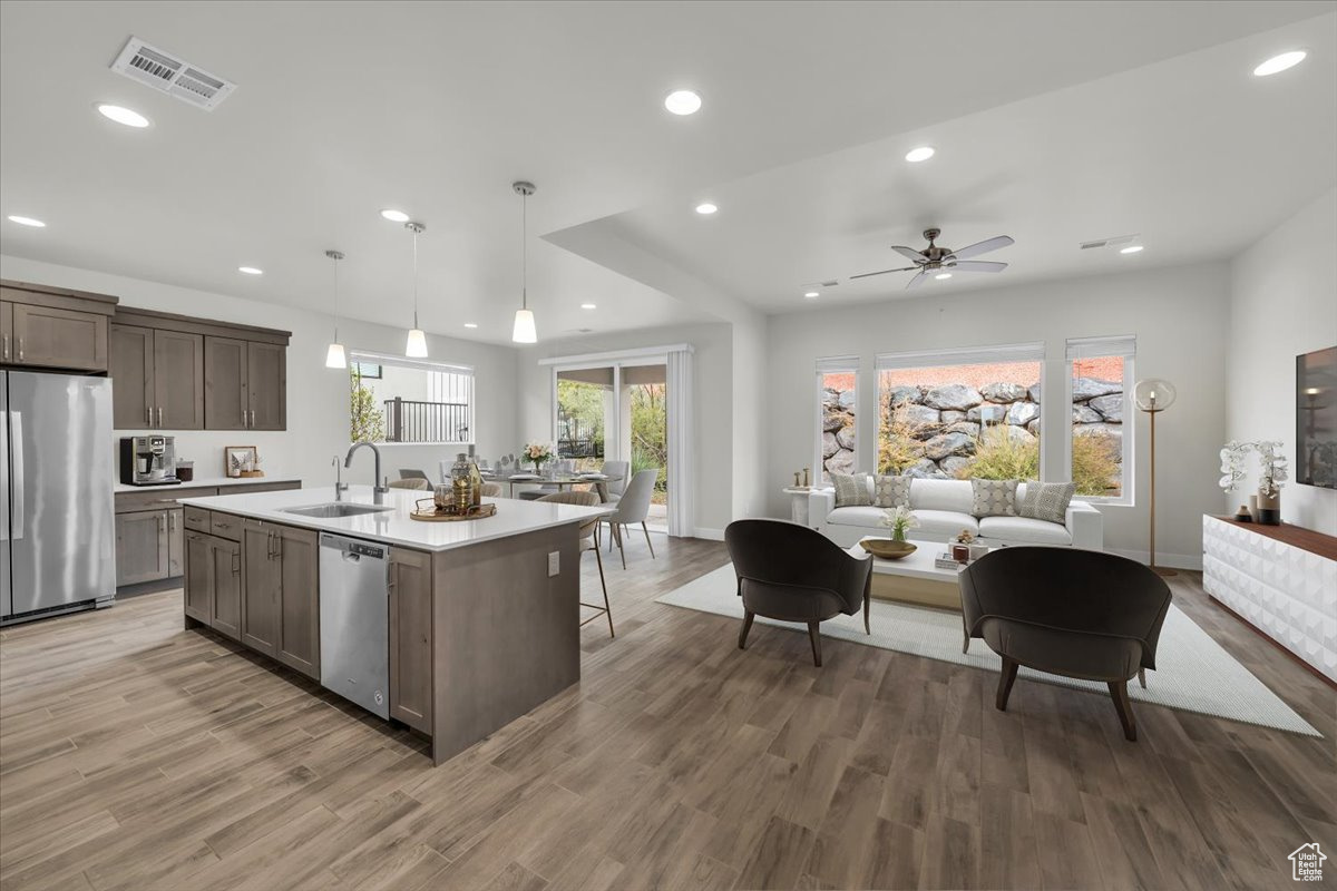 Kitchen with appliances with stainless steel finishes, sink, decorative light fixtures, a center island with sink, and hardwood / wood-style floors