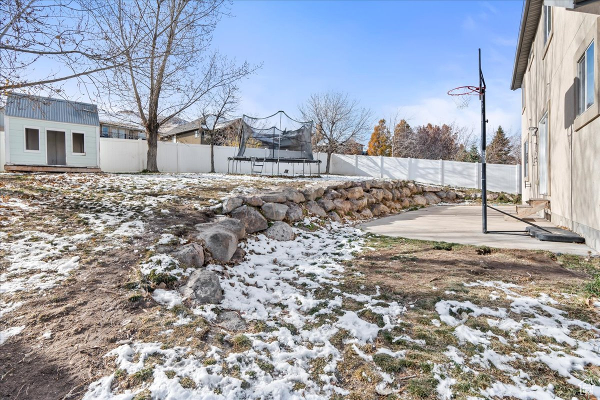 Snowy yard featuring an outbuilding, a trampoline, and a patio