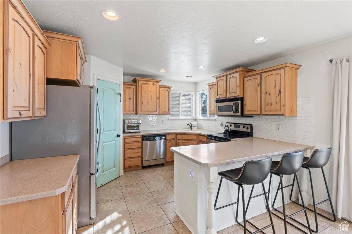 Kitchen with kitchen peninsula, a kitchen bar, stainless steel appliances, sink, and light tile patterned flooring